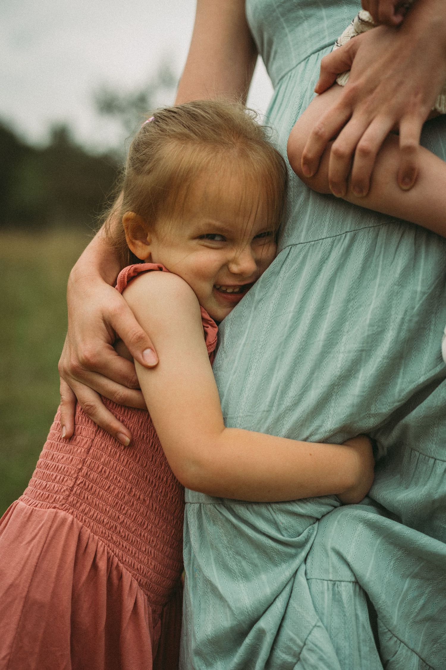 A child in a coral pink dress hugs someone wearing a mint green shirt in a series of tender outdoor moments.