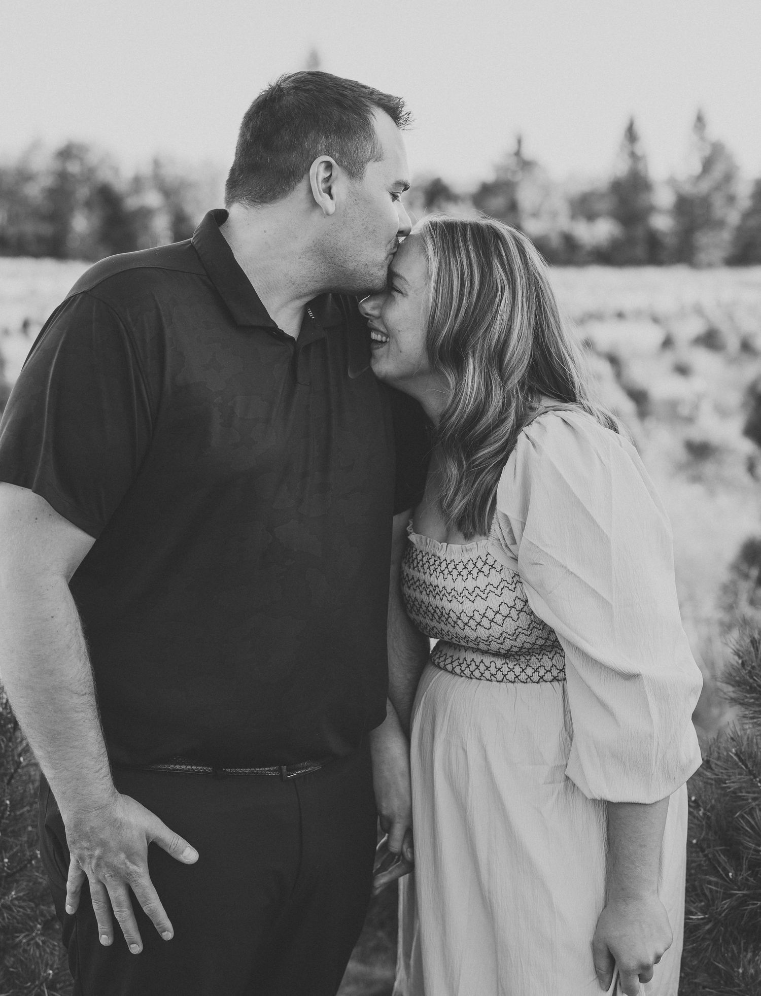 A couple shares an intimate moment in a black and white photo series showing them embracing in an outdoor setting.