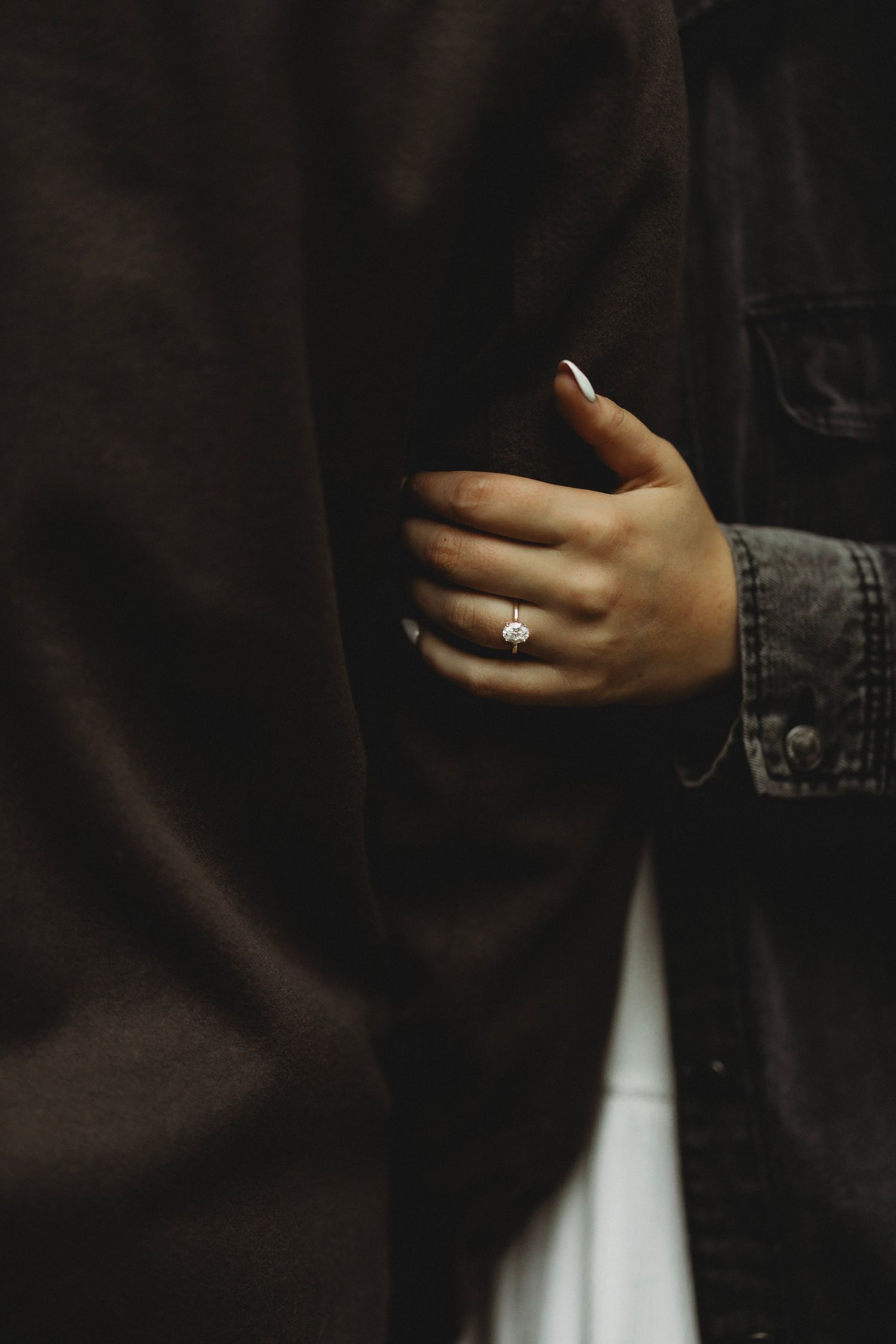 Close-up of a woman's hand with a pink gemstone engagement ring resting on a dark coat.
