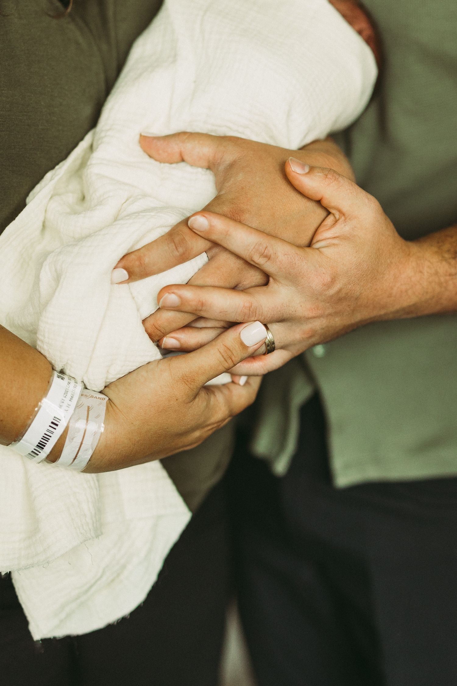 Gentle hands holding newborn baby wrapped in white hospital blanket.