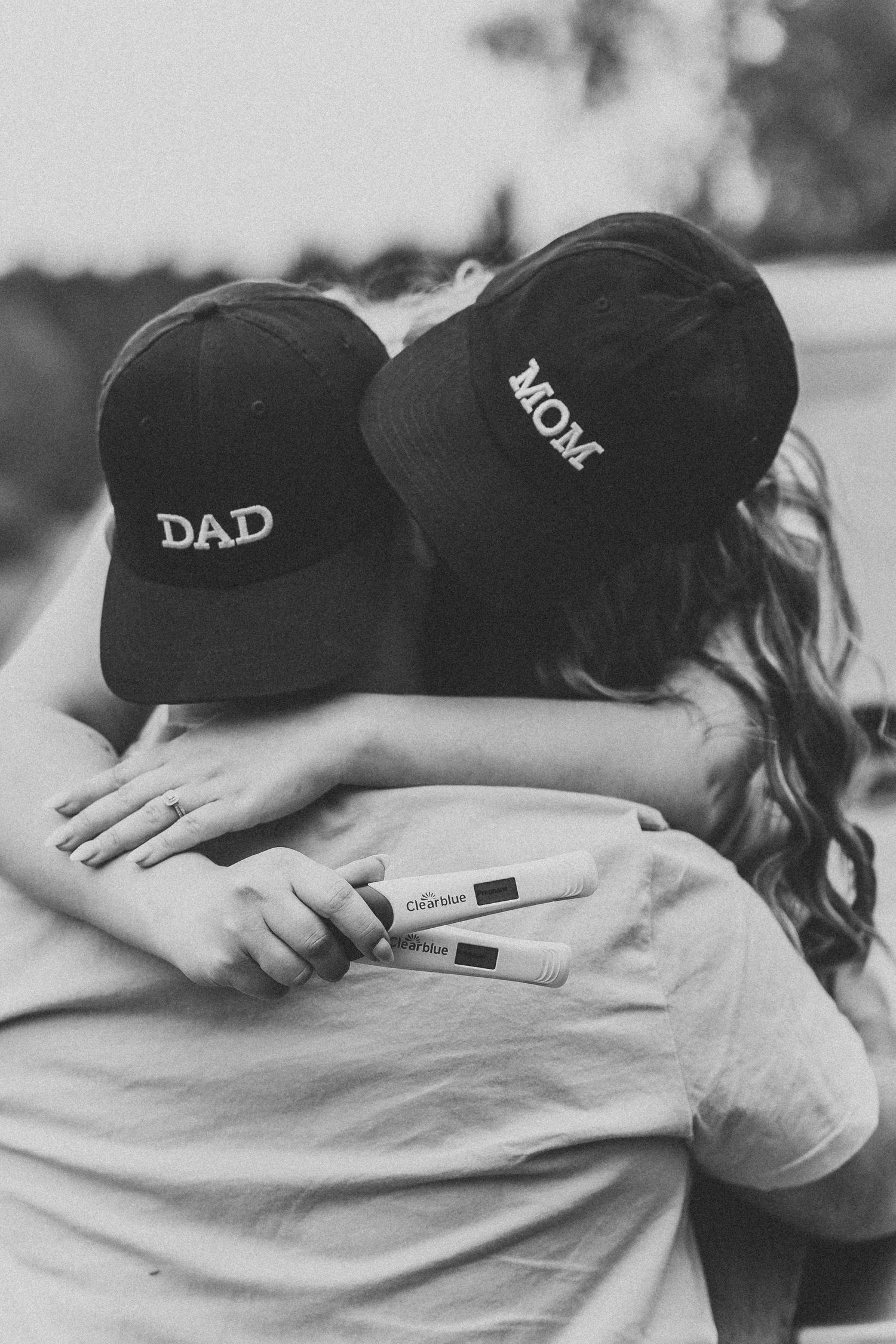 Person wearing 'DAD' baseball cap holding pregnancy test in emotional black and white moment.