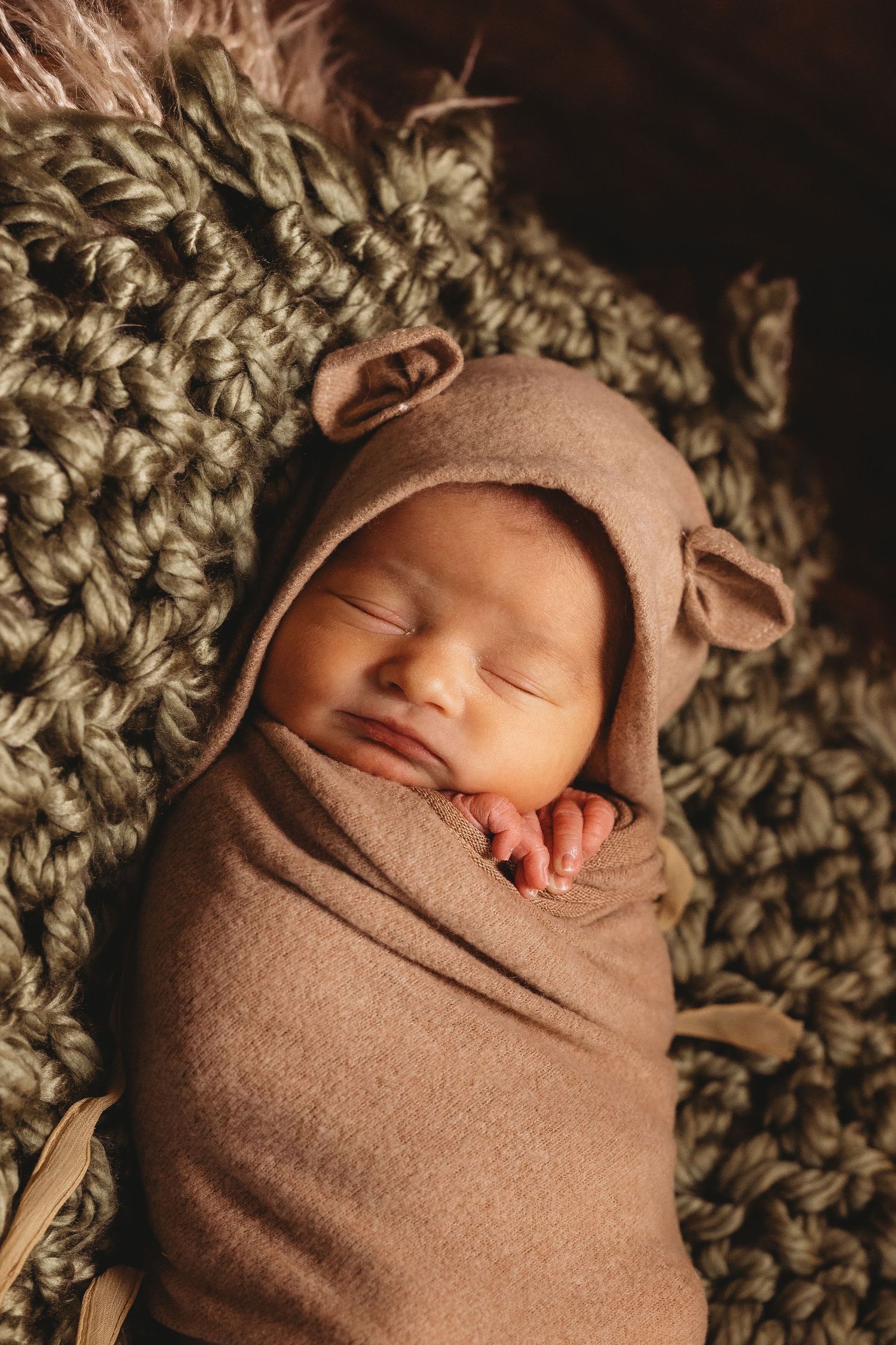 Peaceful newborn sleeping while swaddled in brown wrap on knitted green blanket.
