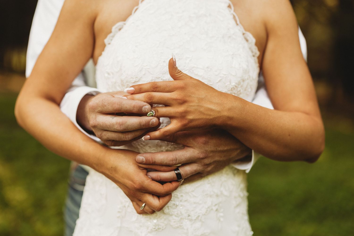 A person wearing a white lace wedding dress holds their hands together in front of their torso.