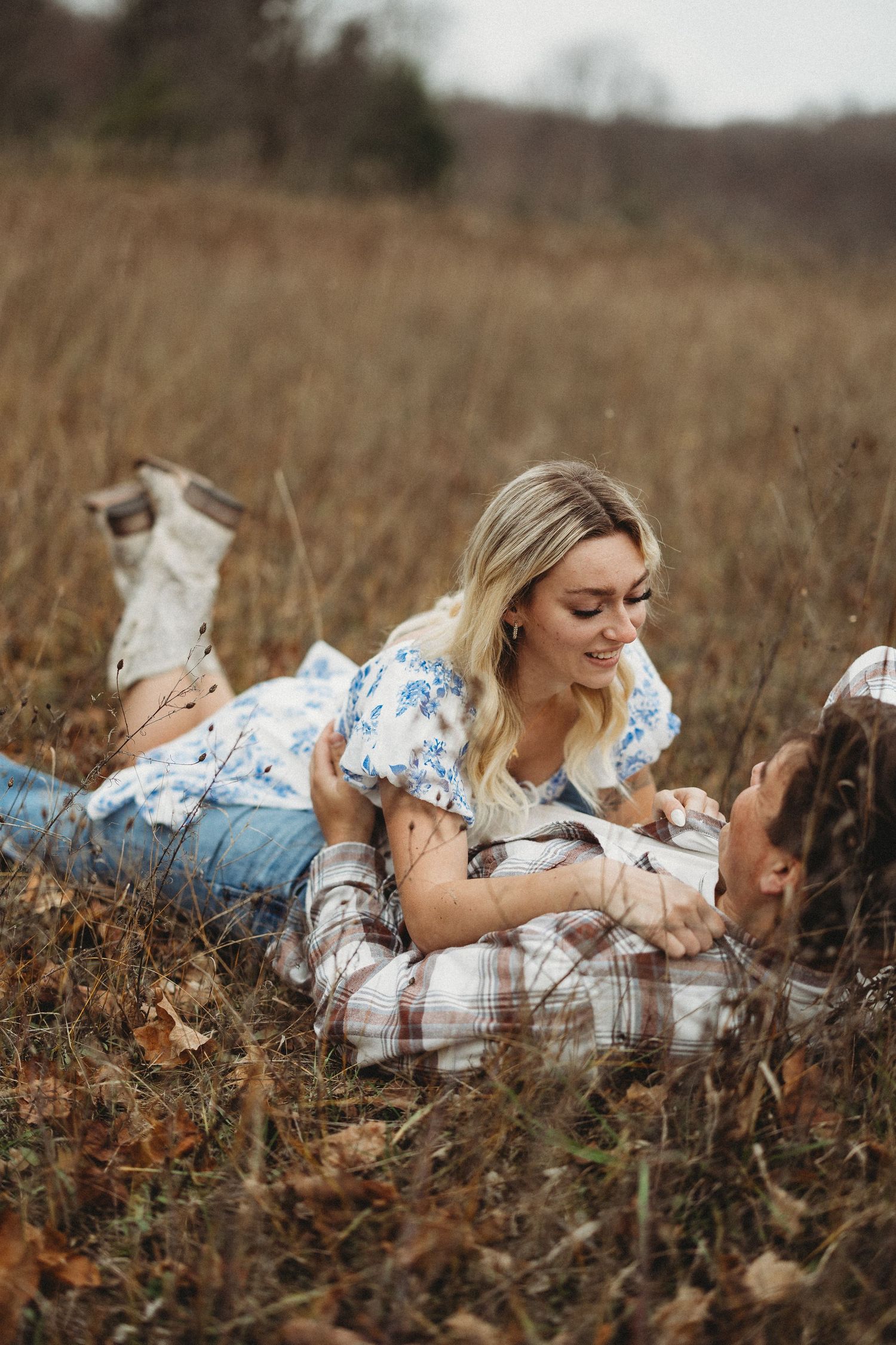 A couple relaxes in a rustic autumn field with their cat while wearing casual clothing and plaid.