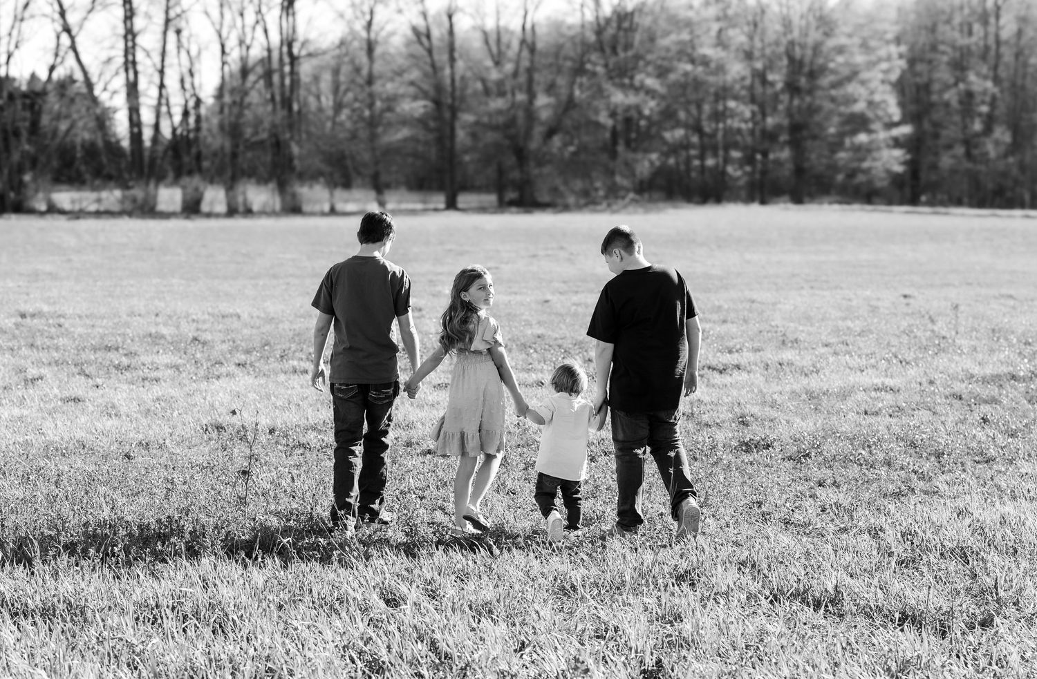 Black and white photo of a family walking through an open field, holding hands with a toddler between them.