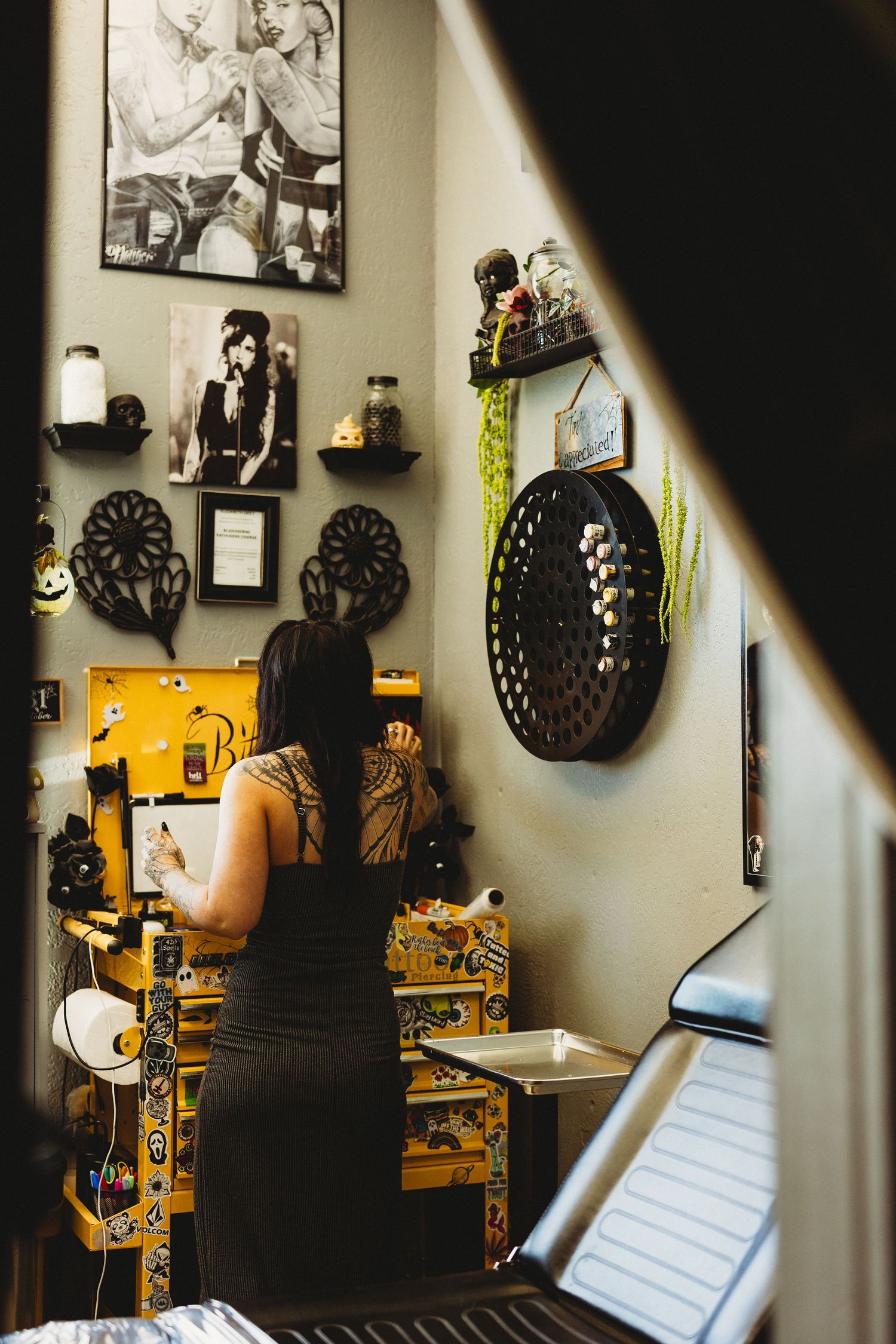 Tattoo artist working at a decorated yellow station with art and photos on the wall.