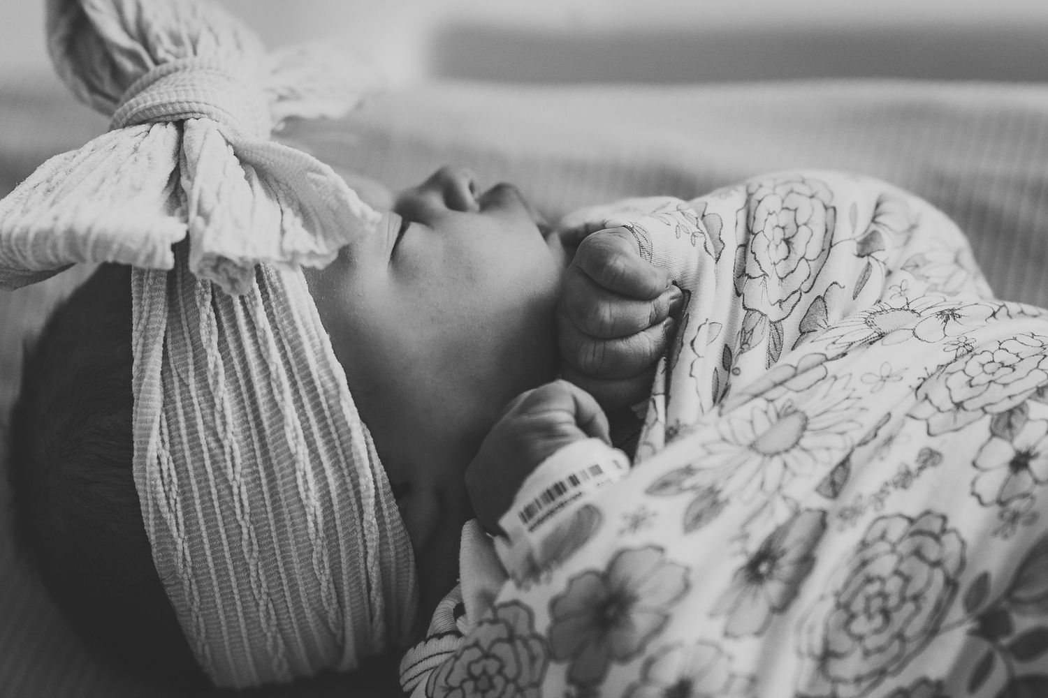 Close-up view of sleeping newborn wrapped in delicate floral swaddle.