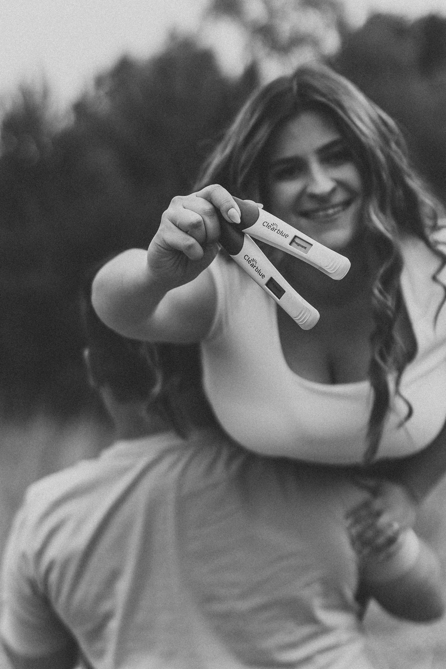 Person holding up positive pregnancy test sticks in black and white photo.