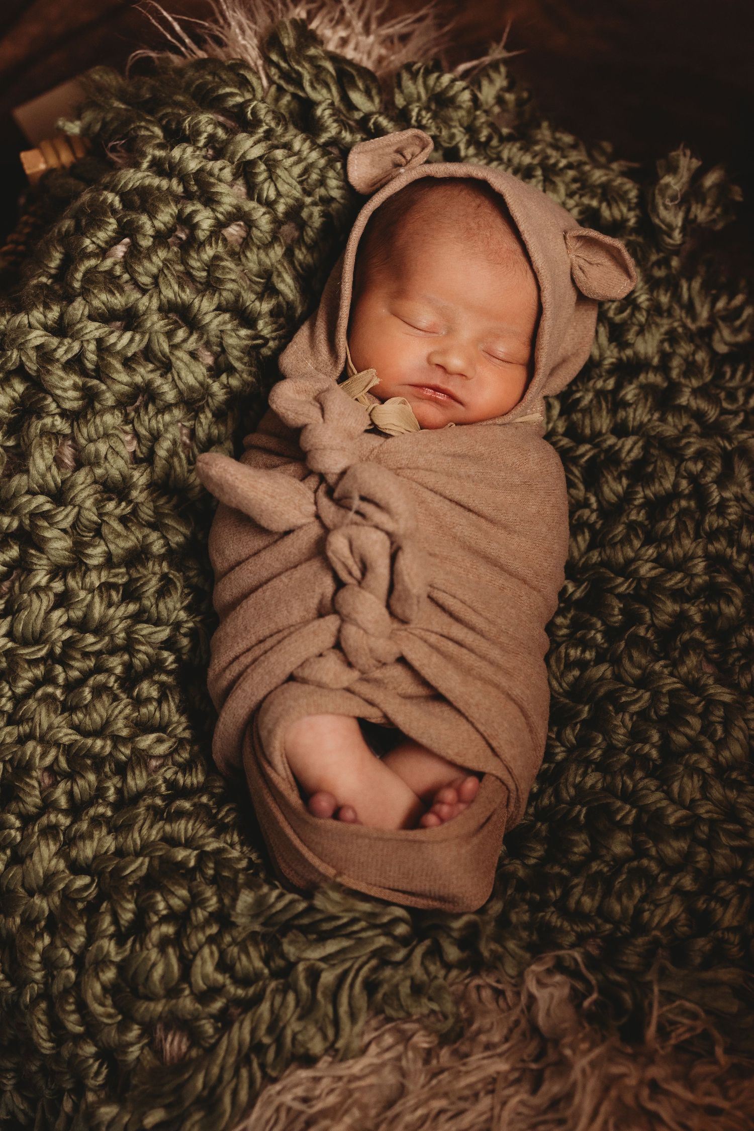 Sleeping newborn wrapped in brown swaddle on textured green blanket.