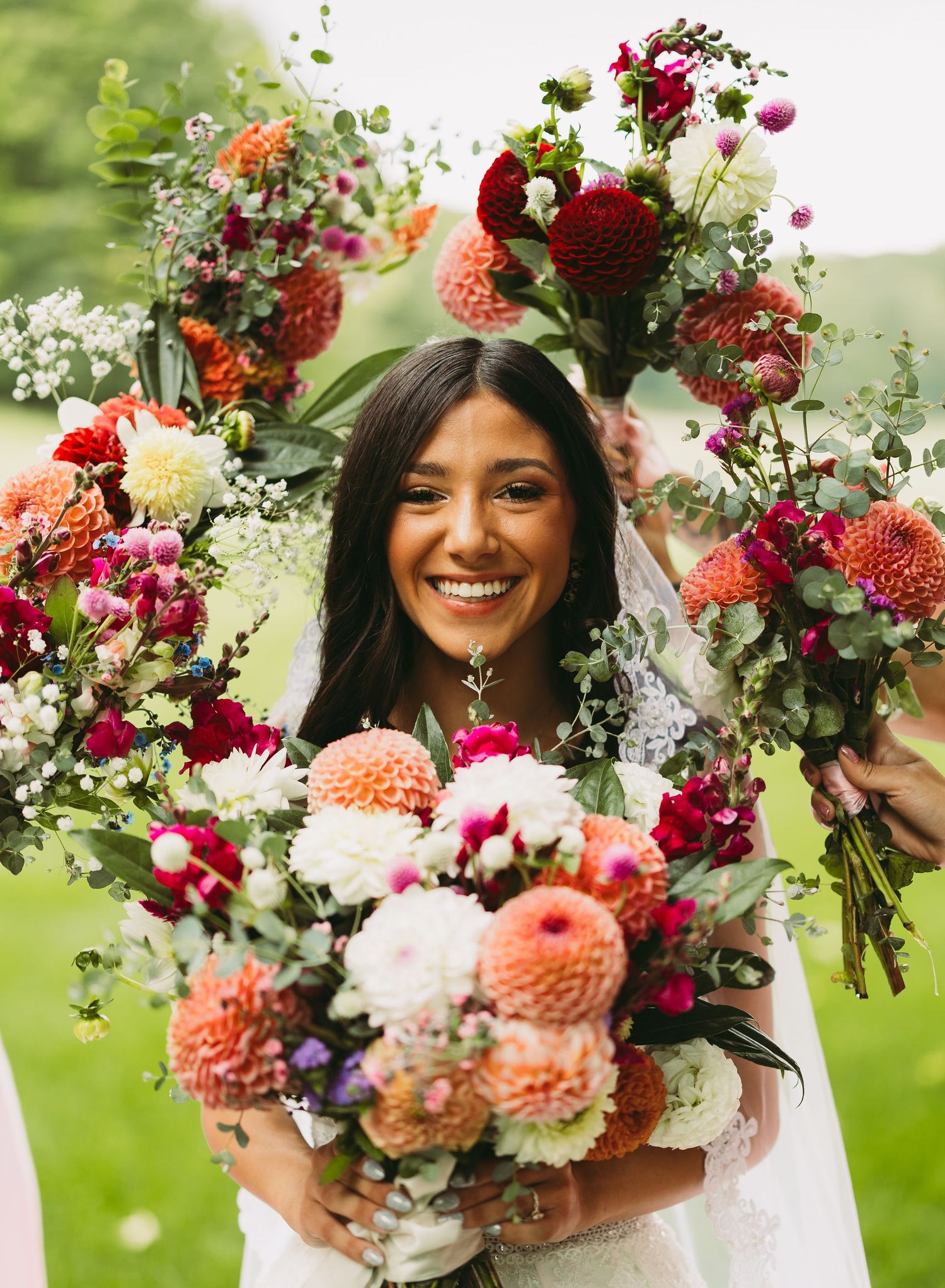 Vibrant floral bouquet with coral dahlias, burgundy flowers and greenery against an outdoor backdrop.