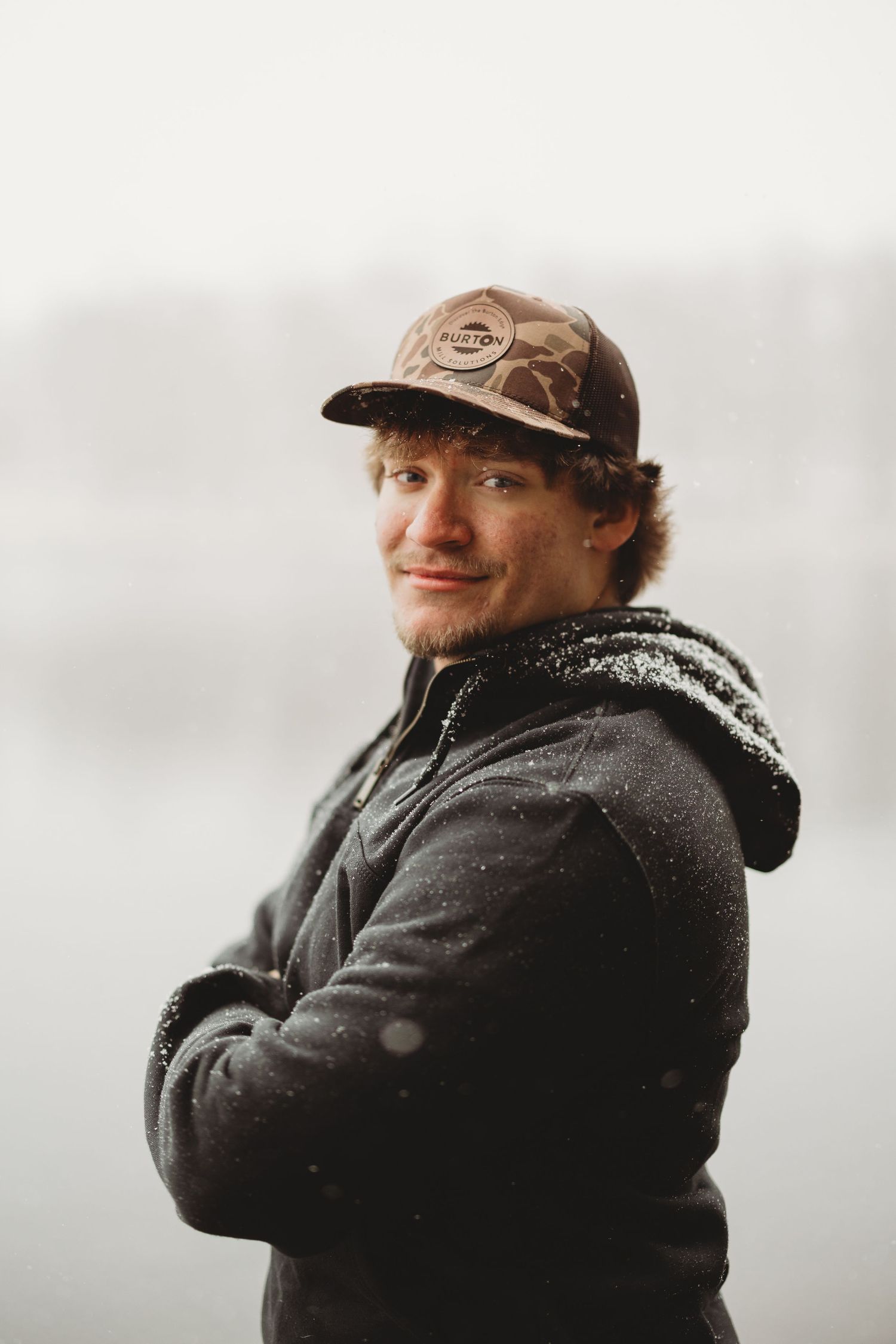 Person wearing baseball cap and hoodie smiling at camera.