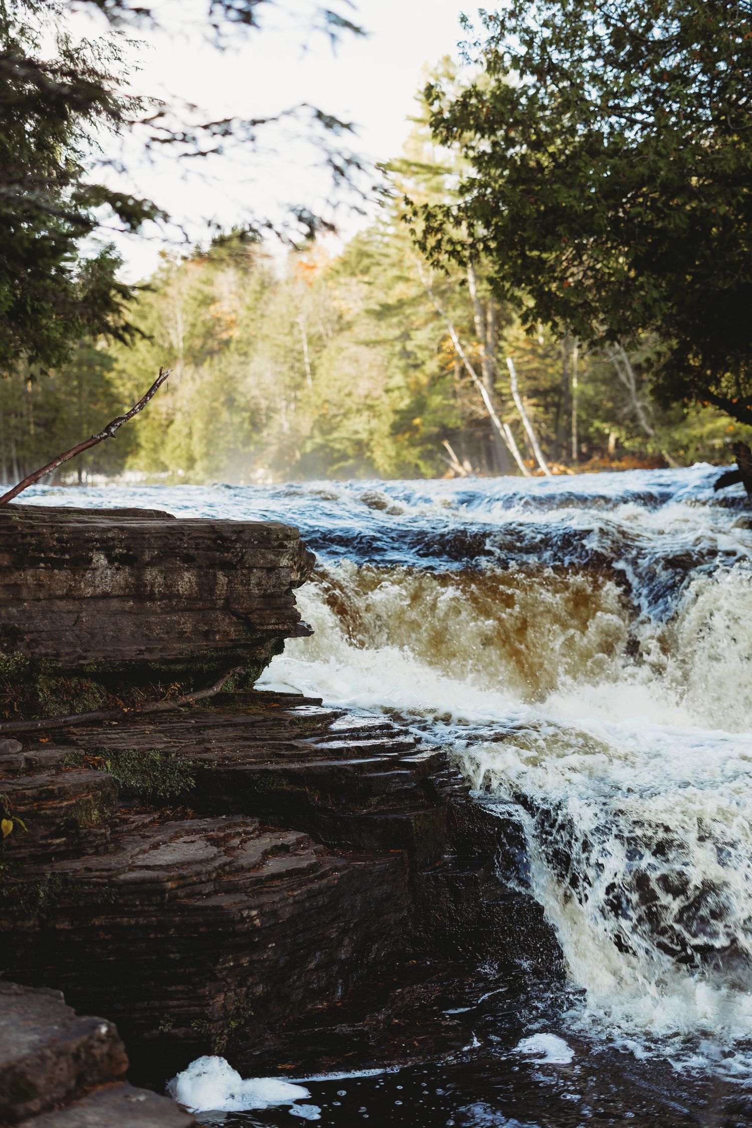 Rushing waterfall cascading over layered rock formations in a natural forest setting.