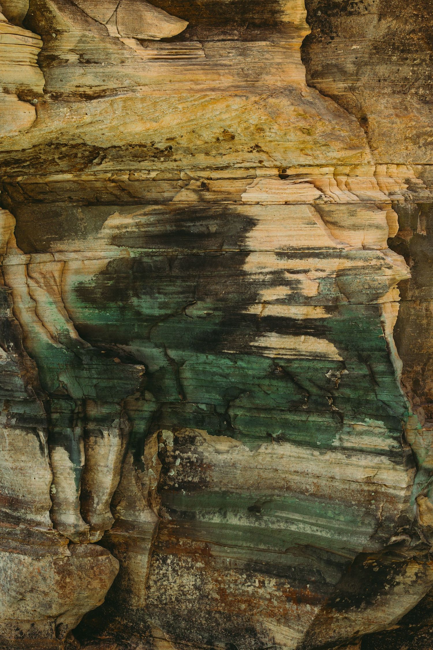 Natural rock formation showing layered sediment patterns in green and brown tones.