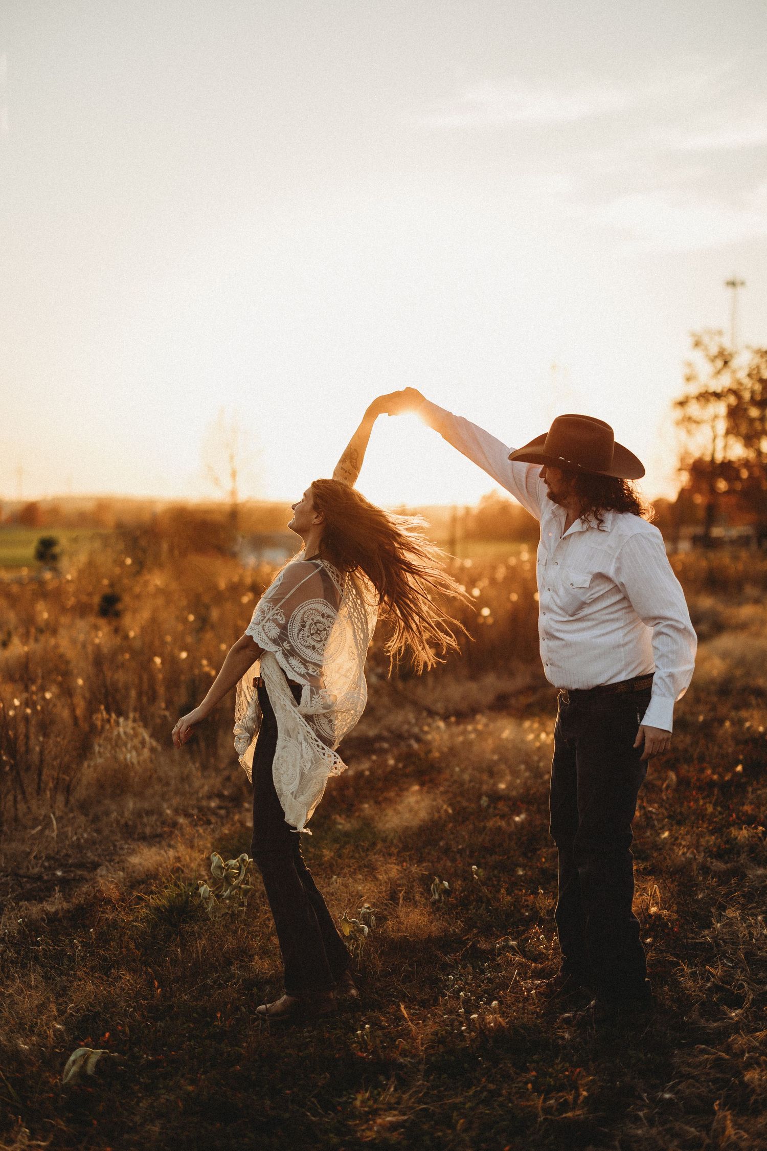 A couple dances together in a field at sunset, creating silhouettes against the golden light.