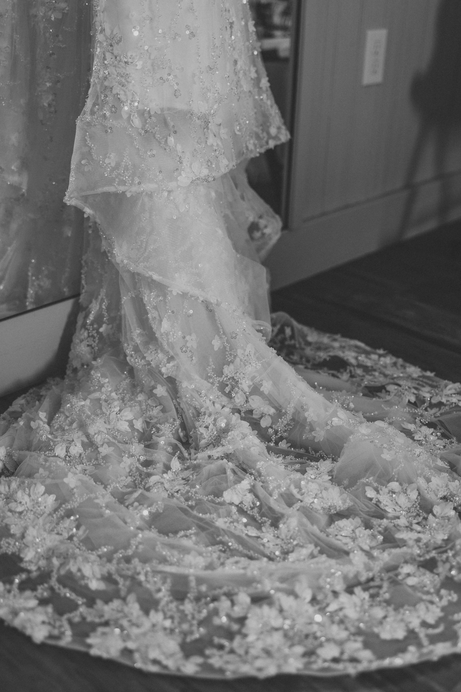 Close-up detail of intricate lace embroidery and beadwork on the hem of a white wedding dress train.