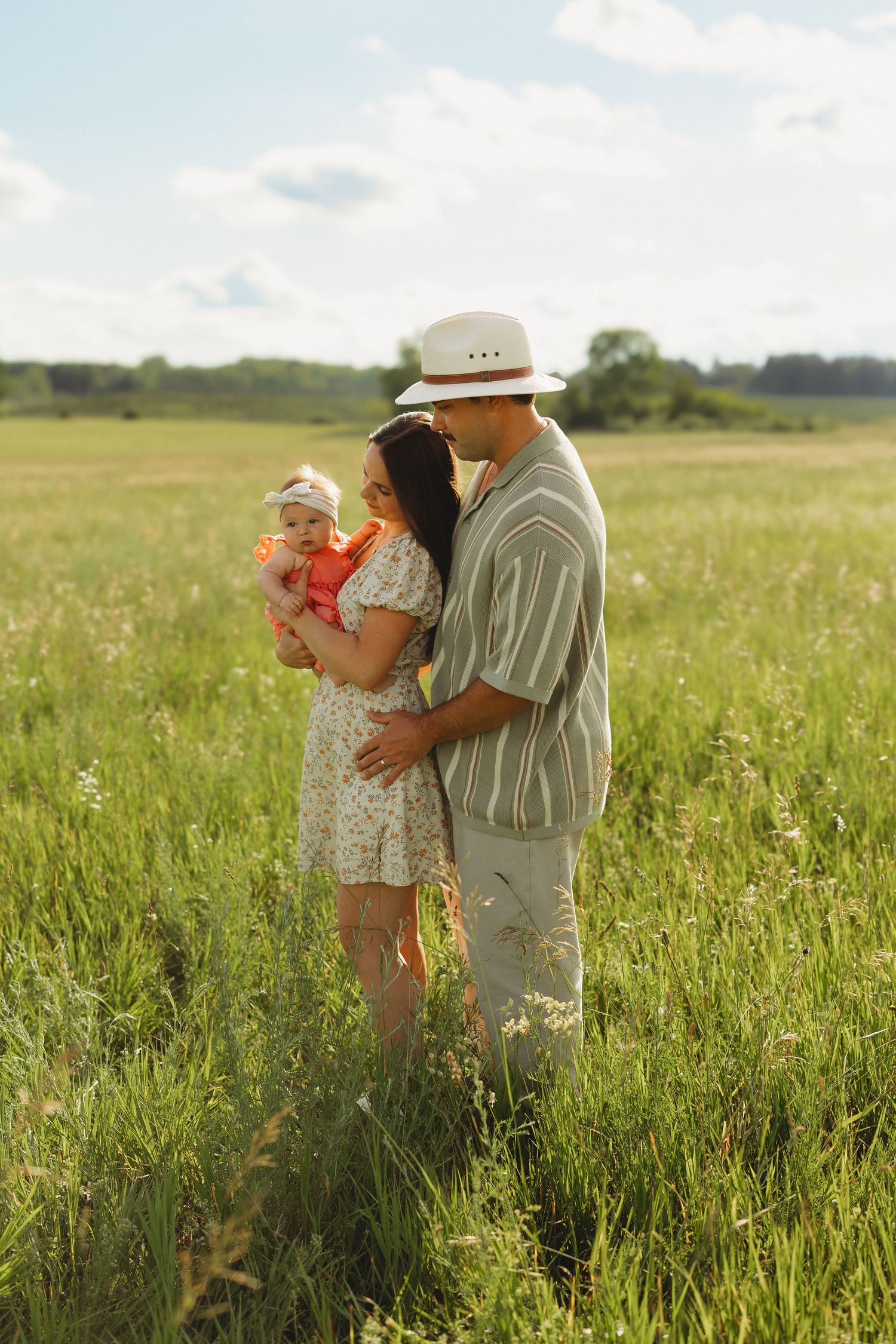 Young couple with infant baby standing in lush green meadow on a sunny summer day.