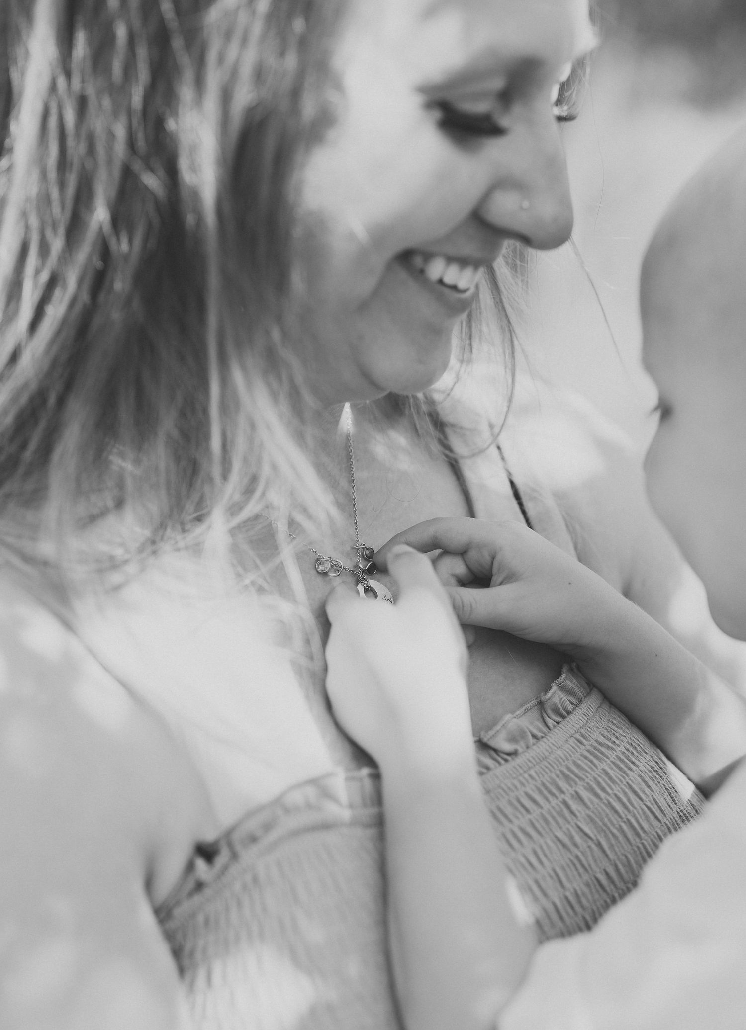 Black and white photo of a smiling woman as a child touches her necklace pendant outdoors.
