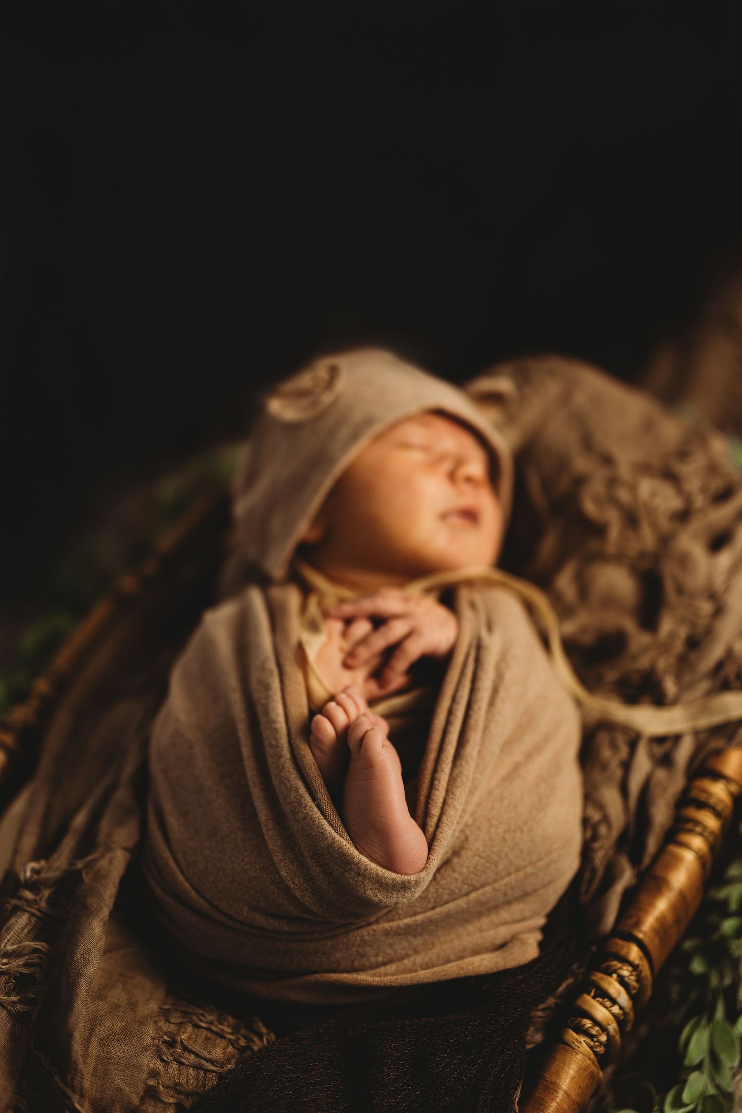 Artistic newborn photography with baby wrapped in neutral tones against dark background.