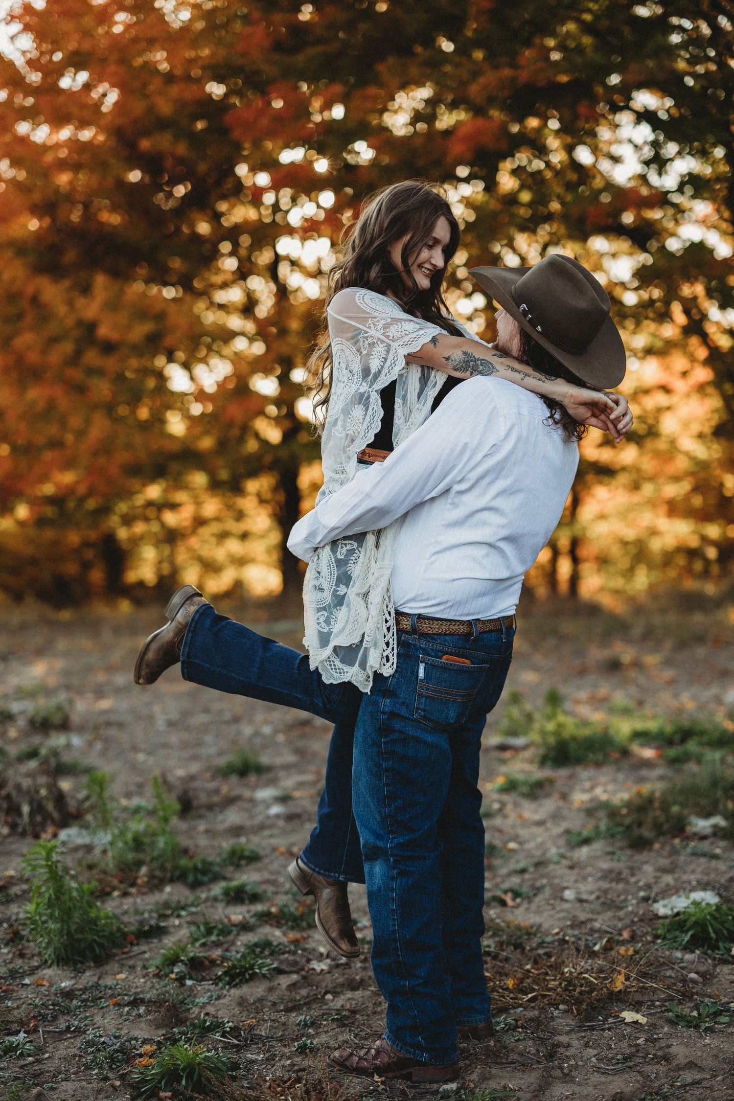 A couple embraces in a romantic moment against a backdrop of autumn trees with golden sunset lighting.
