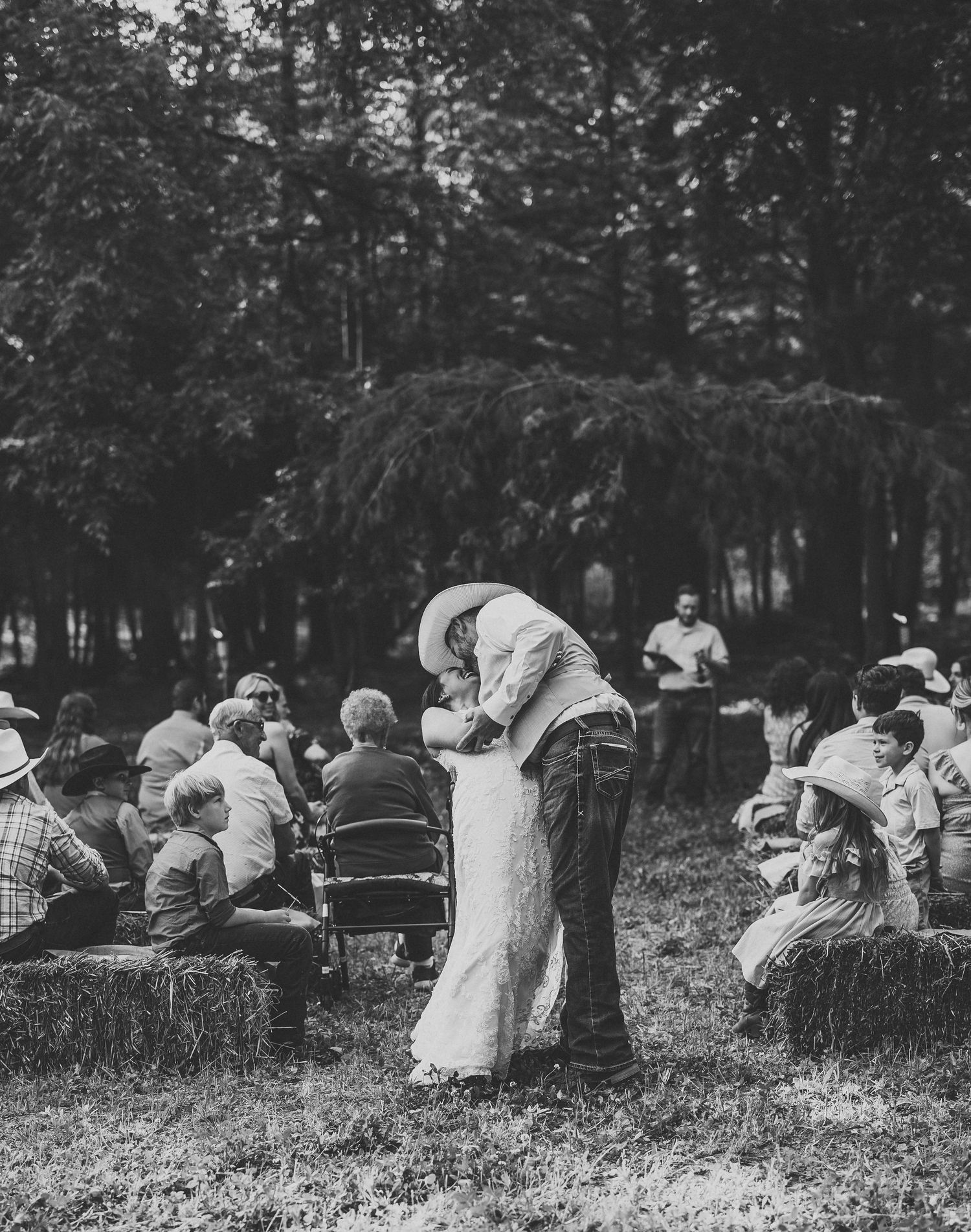 Black and white photo of wedding guests seated outdoors during a forest ceremony.