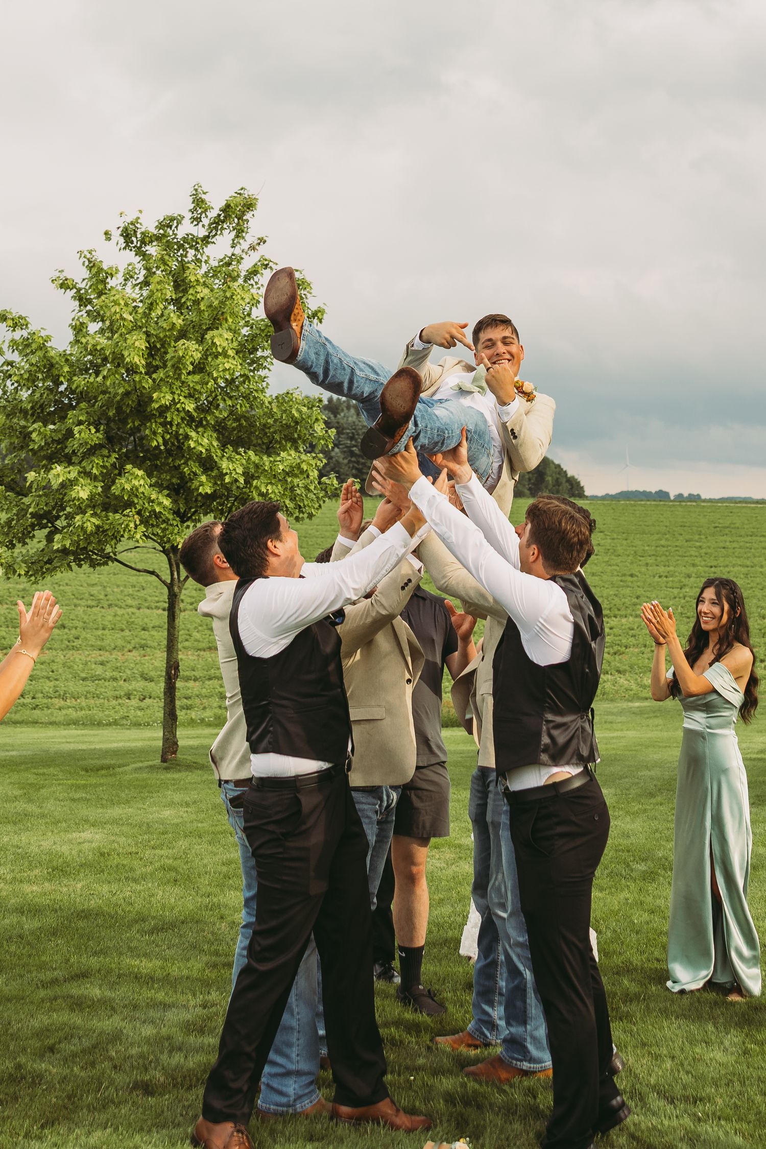A group of people take shots together outdoors on a grassy field with trees in the background.