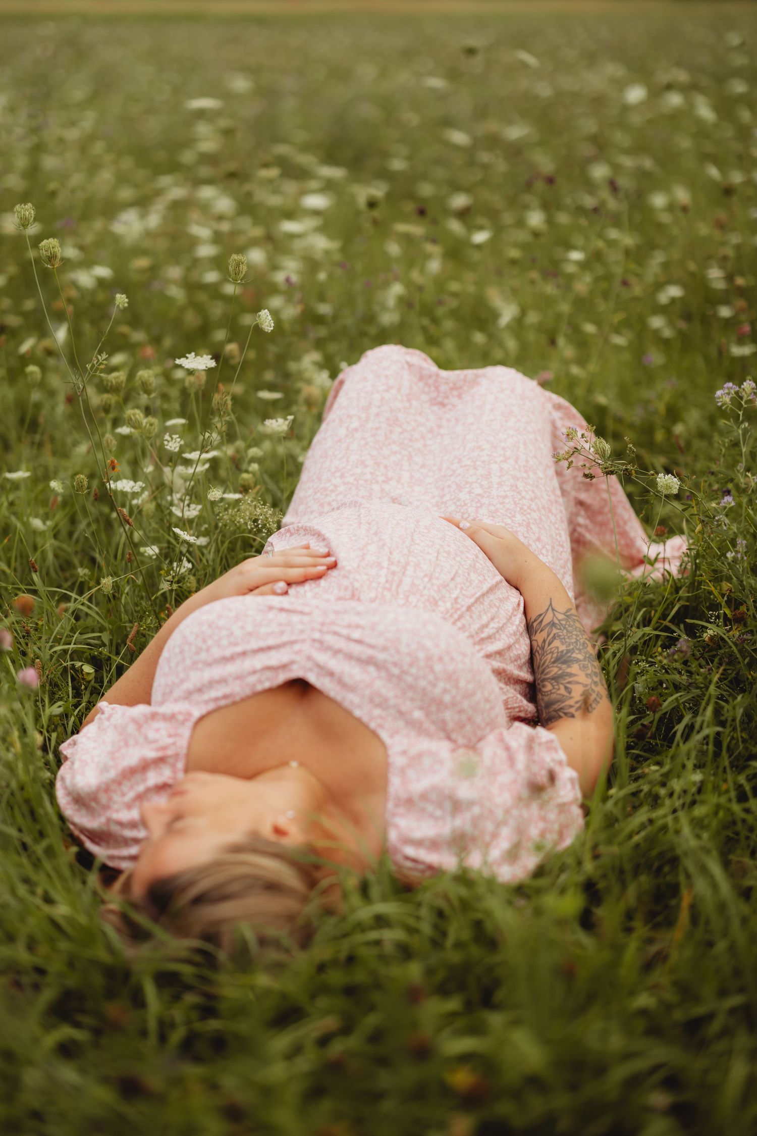 Woman in pink floral dress lying in a wildflower meadow, relaxing among green grass and white daisies.