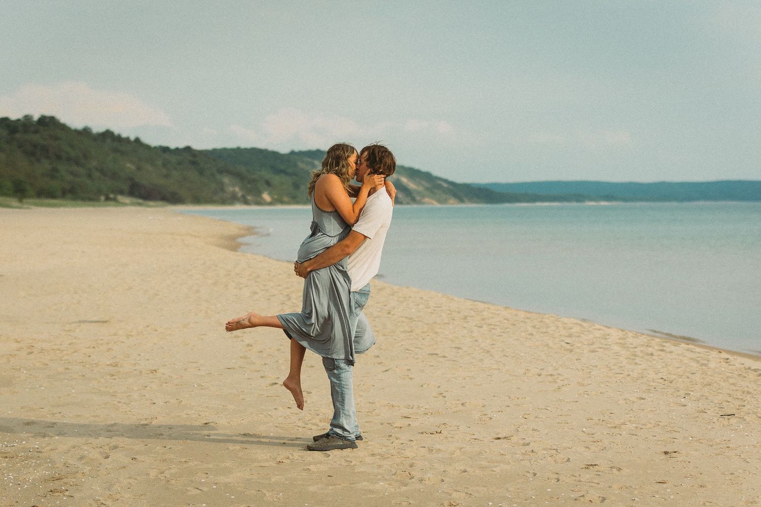 A couple shares intimate moments together on a sunny beach with blue water in the background.