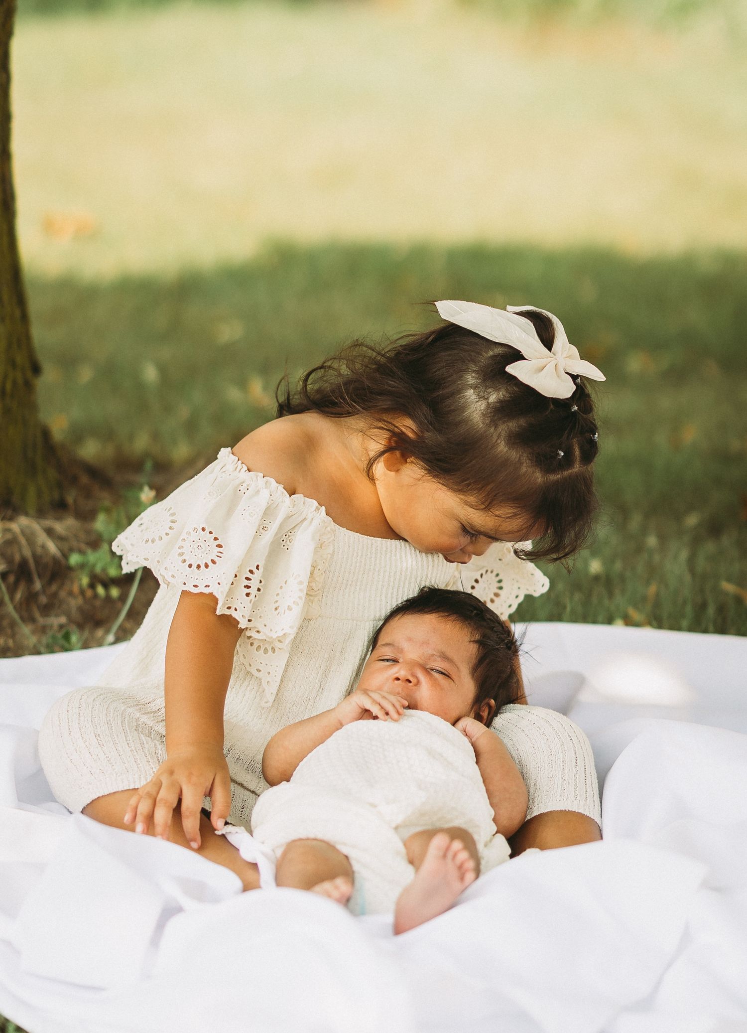 Sweet siblings sharing tender moment on white blanket outdoors.