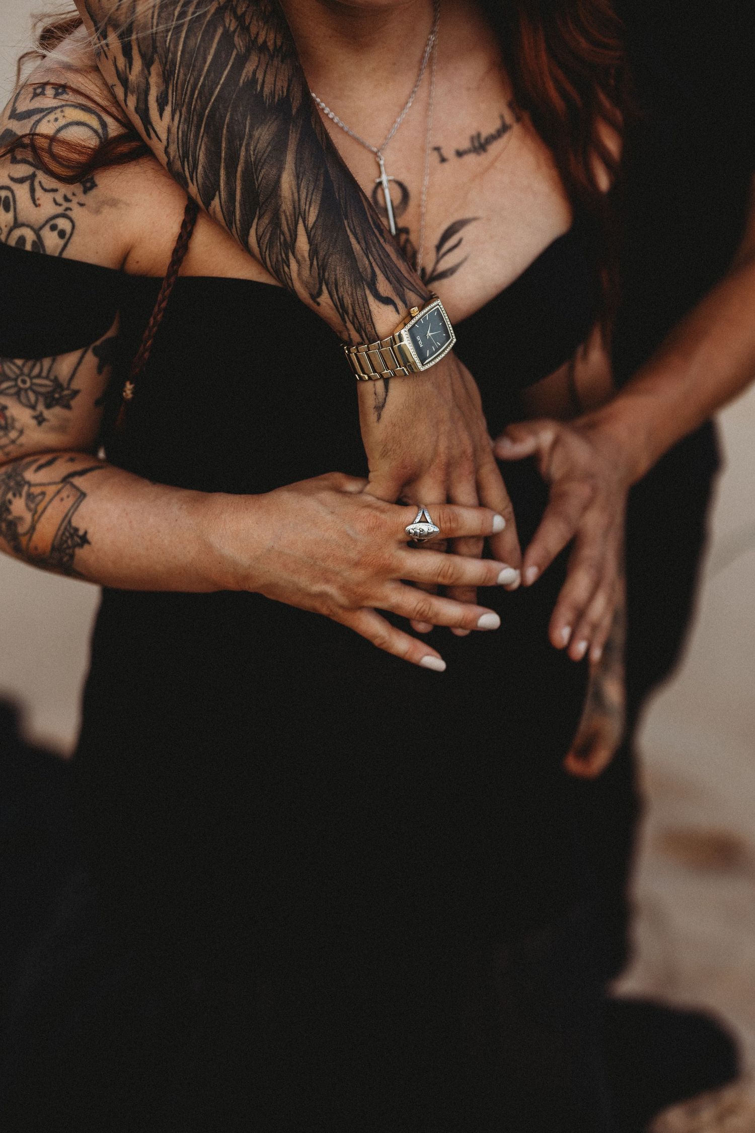 Close-up of tattooed arms and jewelry against black clothing.