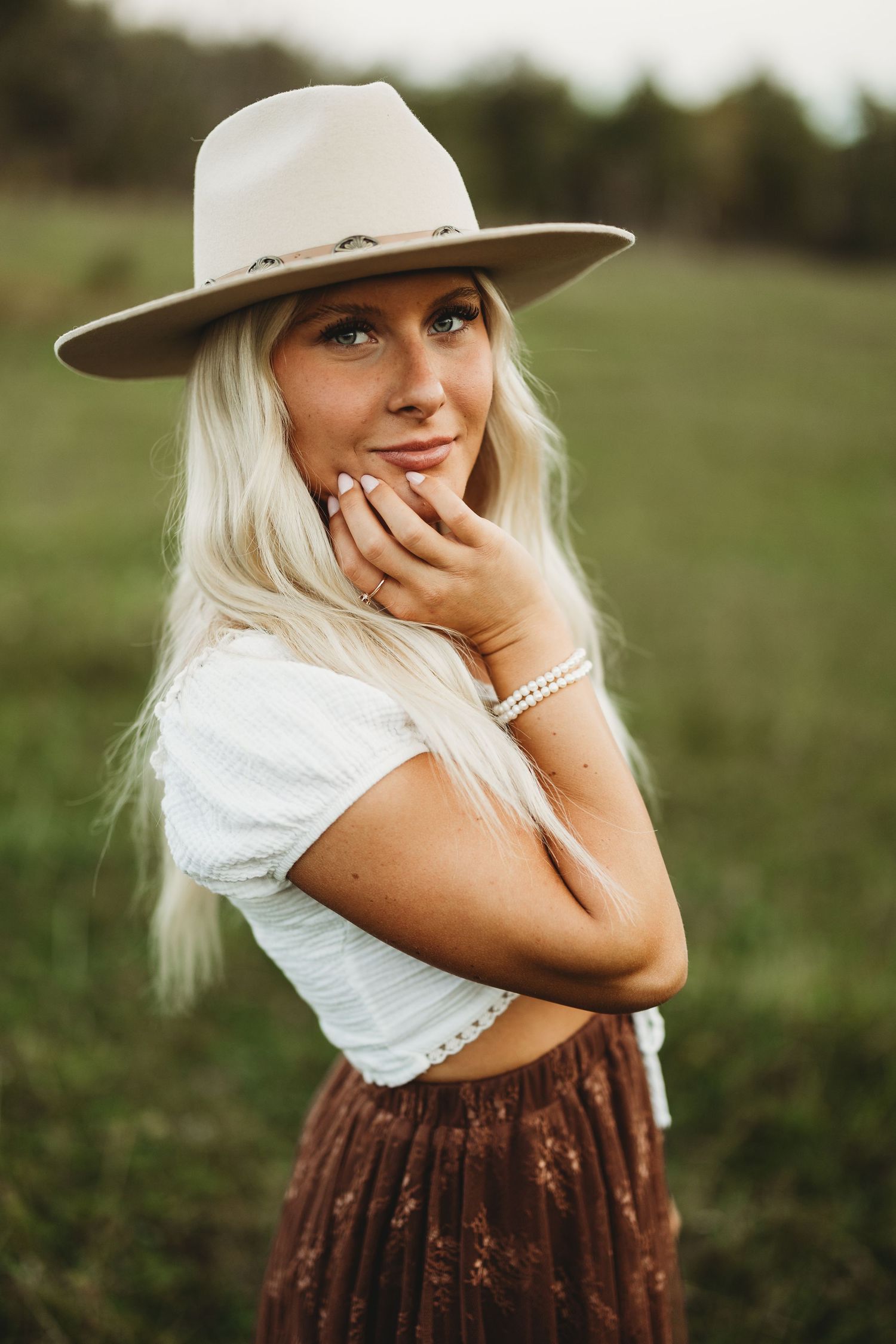 Country style portraits in field wearing white top and cowboy hat with playful poses.