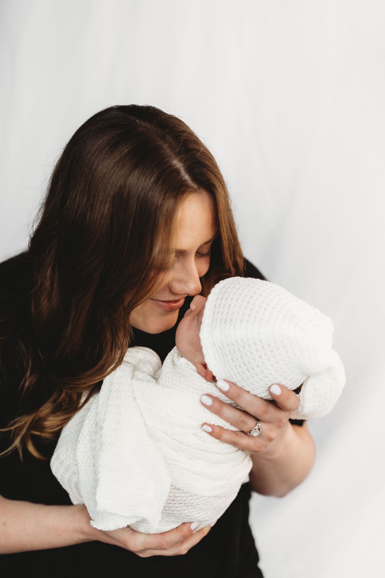 A series of intimate photographs showing tender moments with a white swaddled newborn against a light background.
