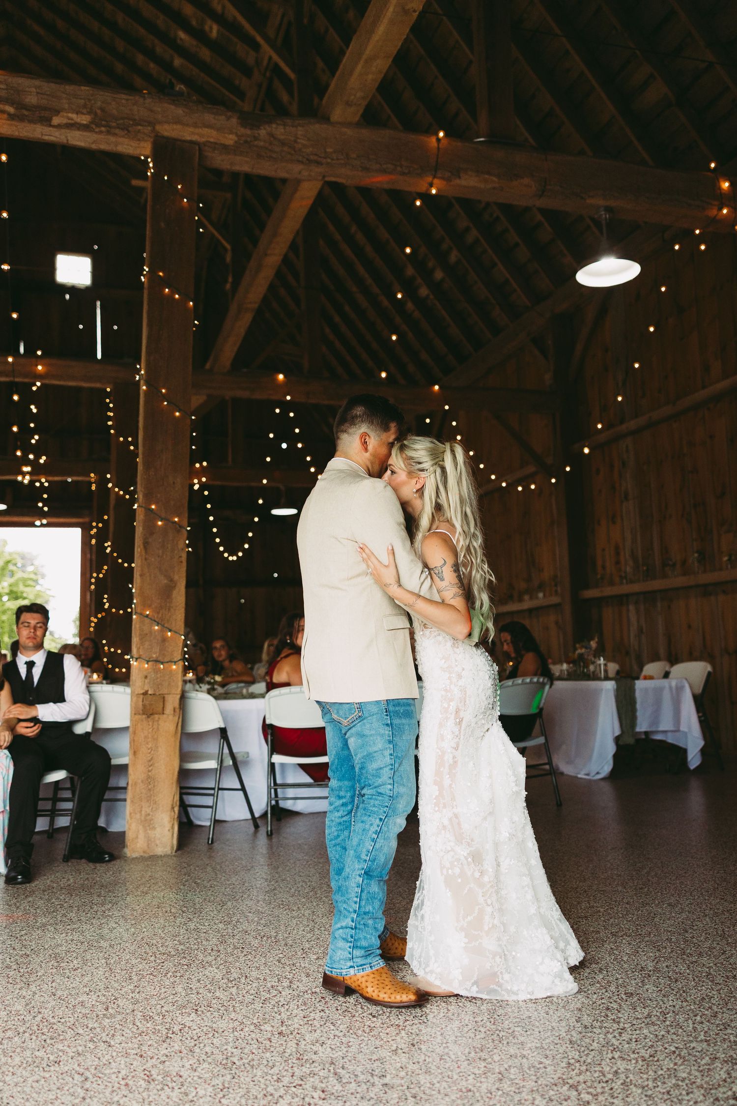 Couple shares a romantic first dance in a rustic barn venue decorated with twinkling string lights.