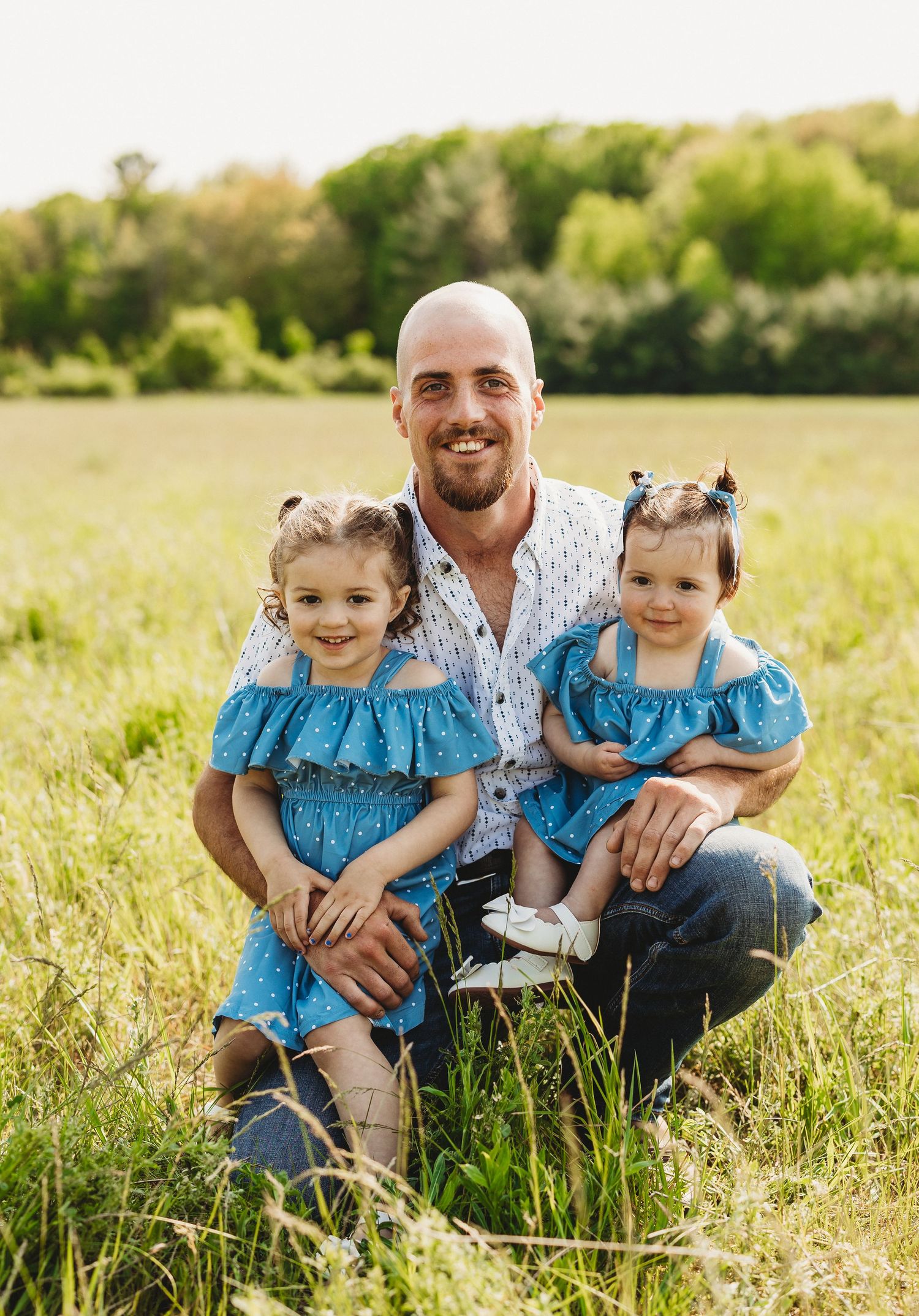 A family sits together in a sunny meadow wearing coordinating blue and white outfits during a summer photoshoot.