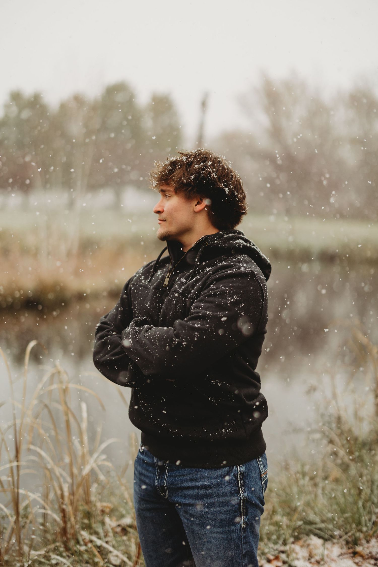 Person standing in snowy field wearing black hoodie and jeans.
