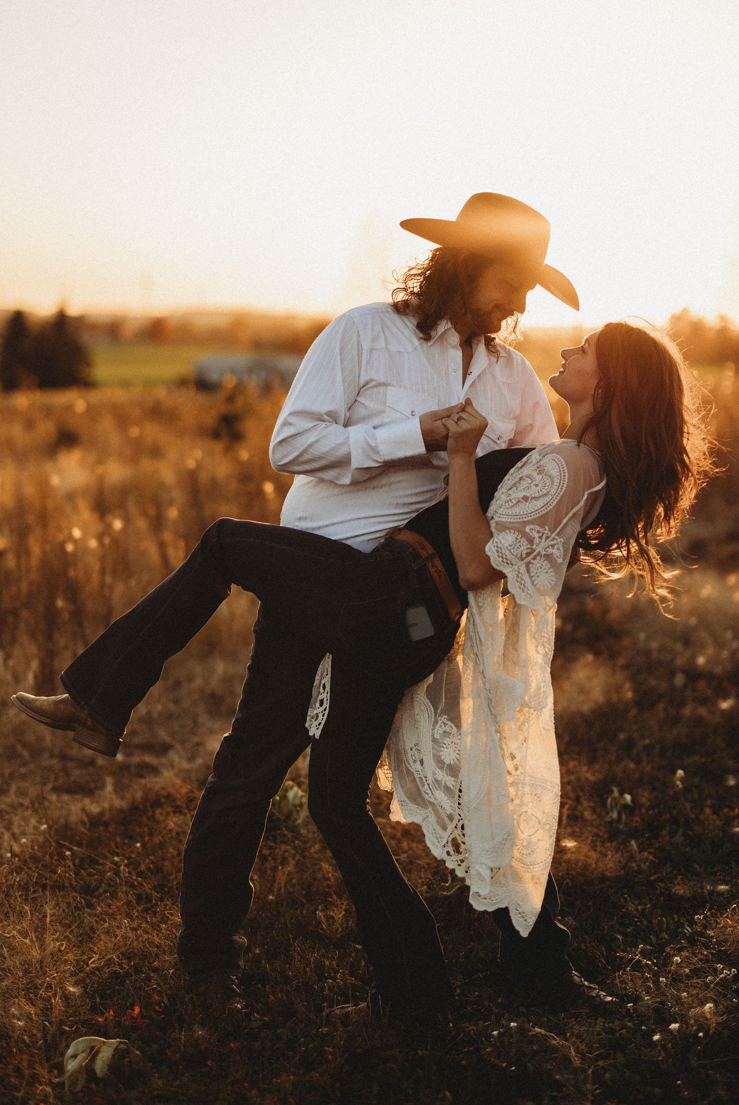A romantic couple in western attire share an intimate moment in a golden field at sunset.