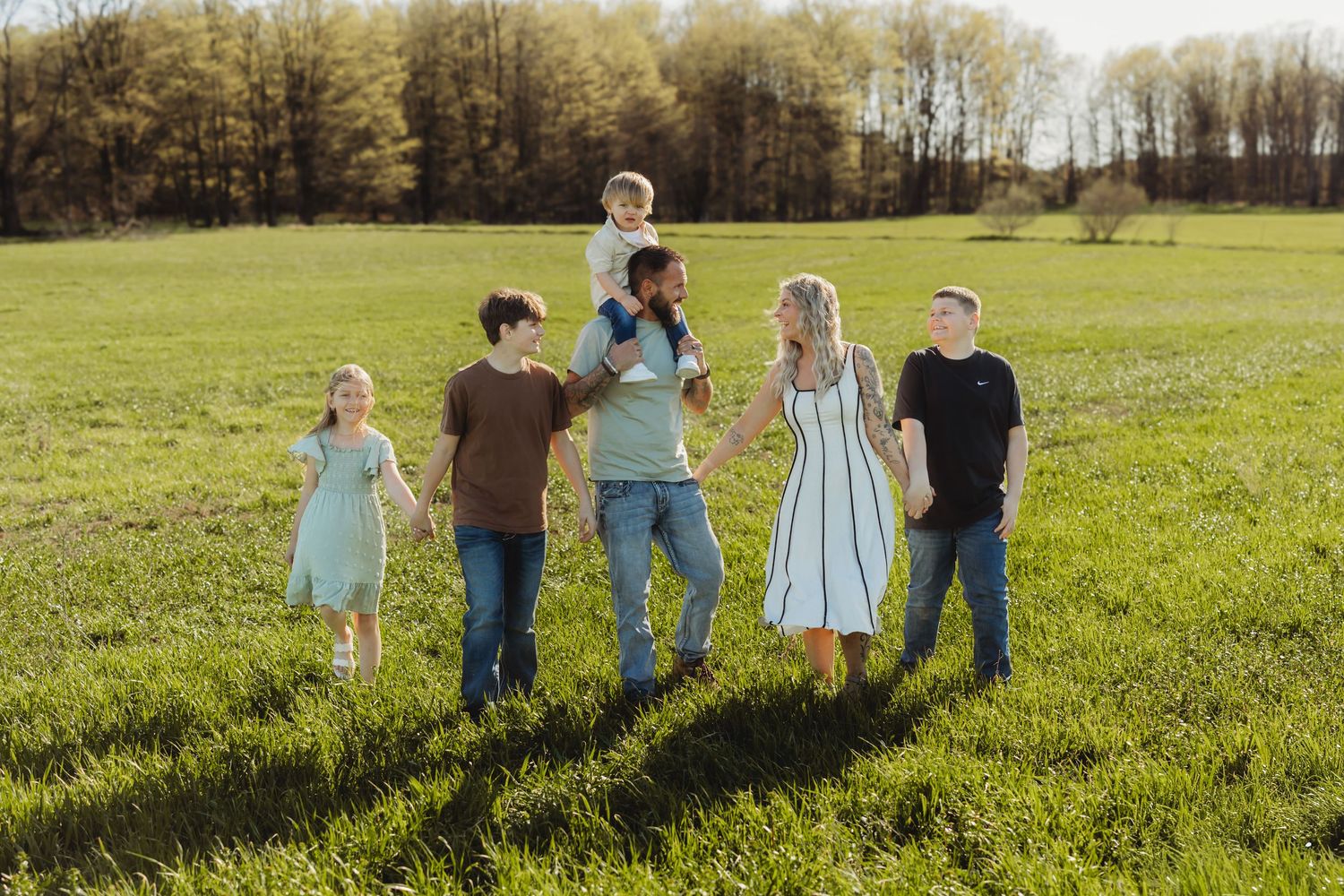 Family of six walking together in a green field on a sunny day, with trees in the background.