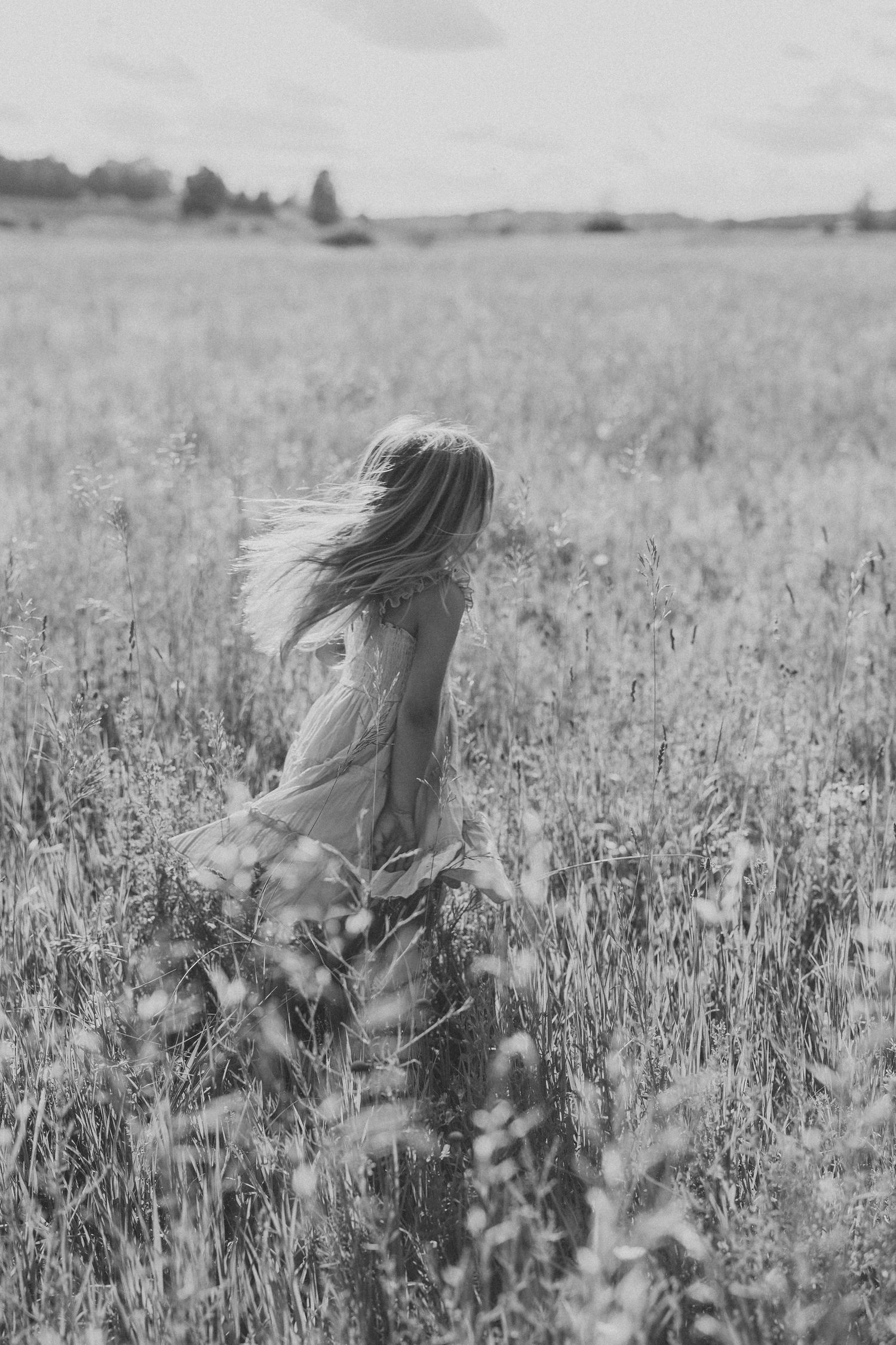 Black and white photo of a woman in a flowing dress running through a wild meadow field with hair blowing in the wind.