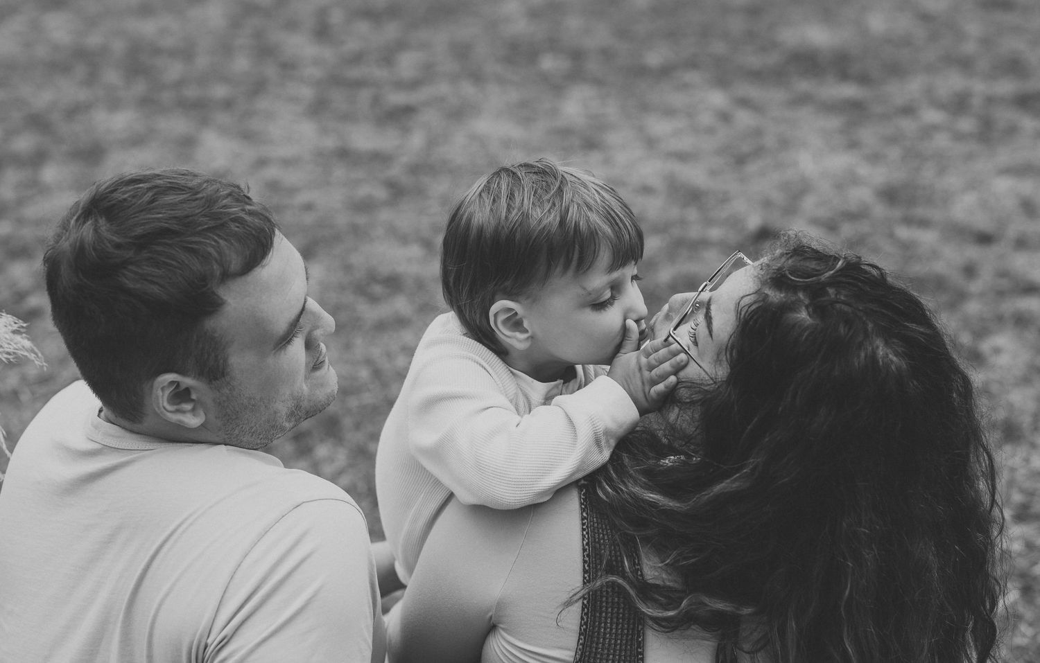 Black and white photo of a young family, with a toddler kissing his mother while father watches lovingly.