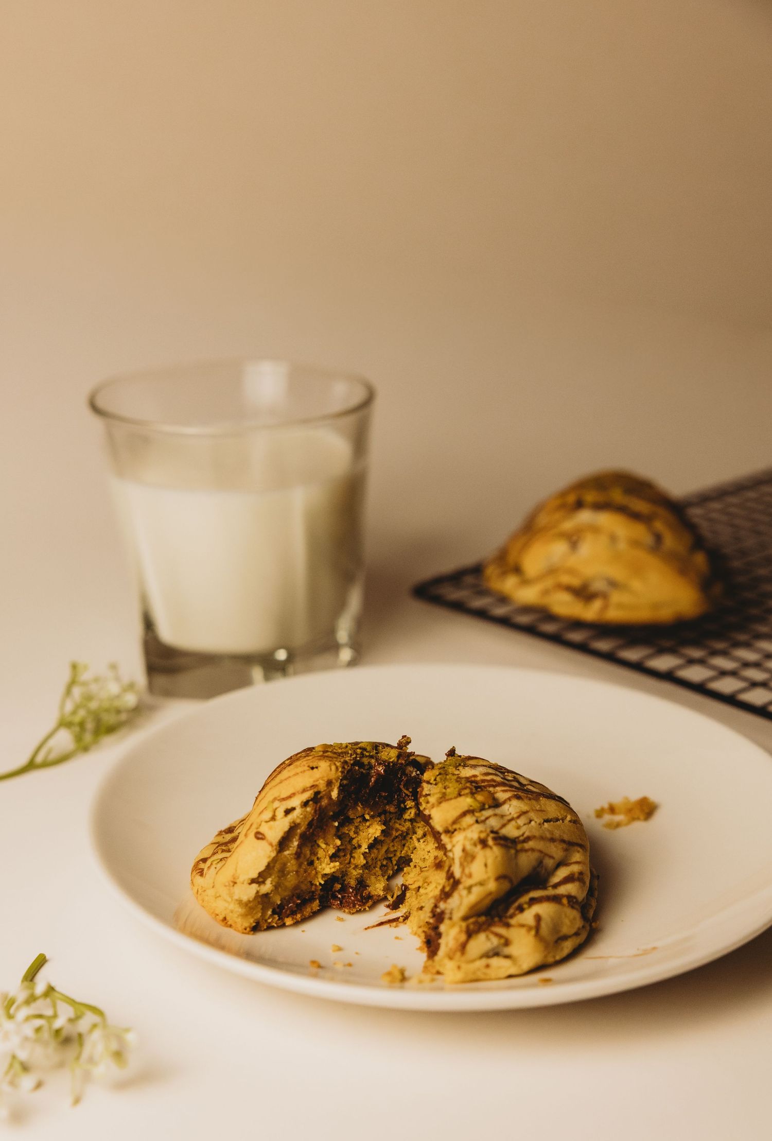Matcha chocolate chip cookie broken in half on a white plate beside a glass of milk and cooling rack.