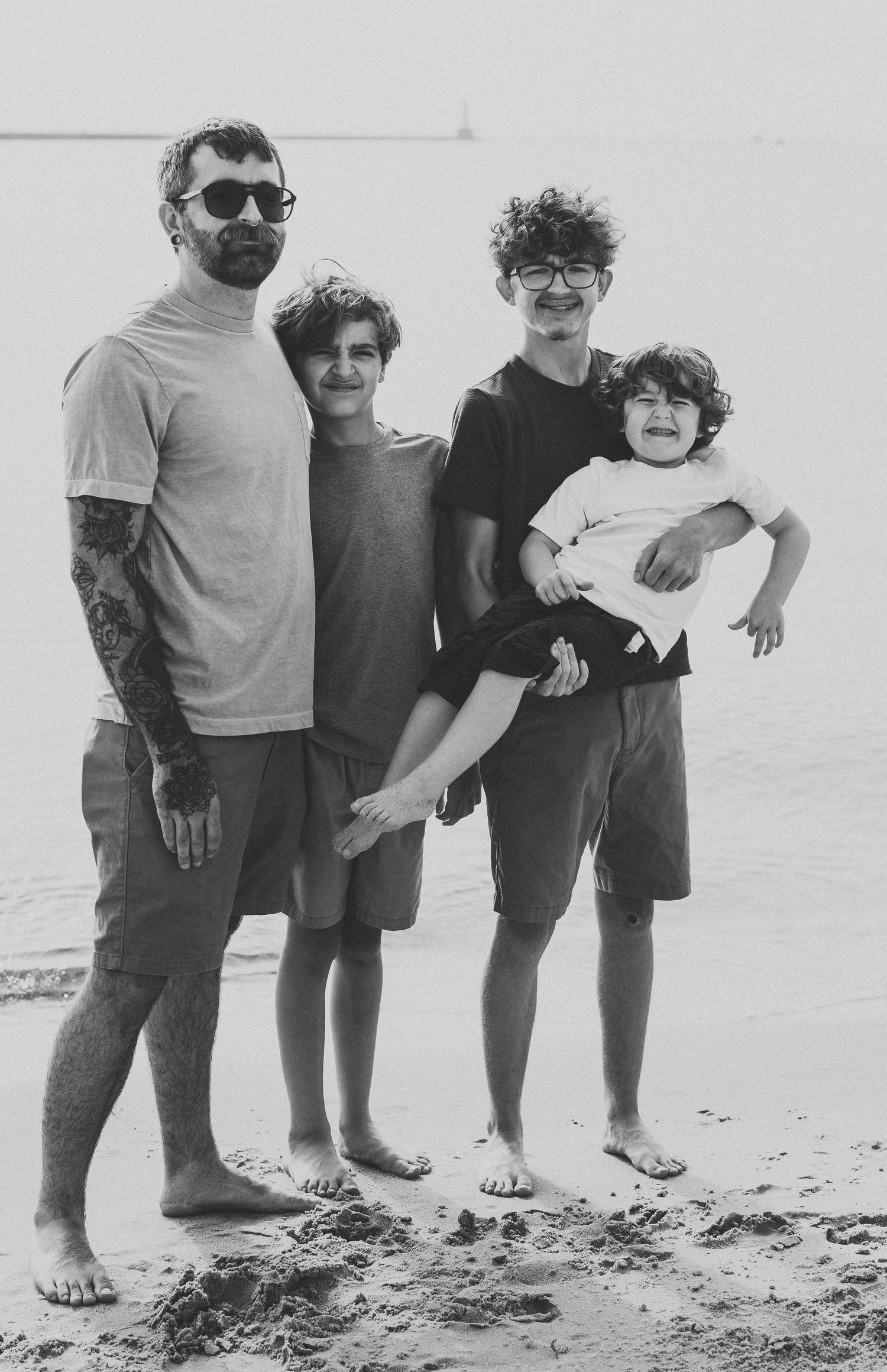 A black and white beach portrait of four people standing together on the sand.