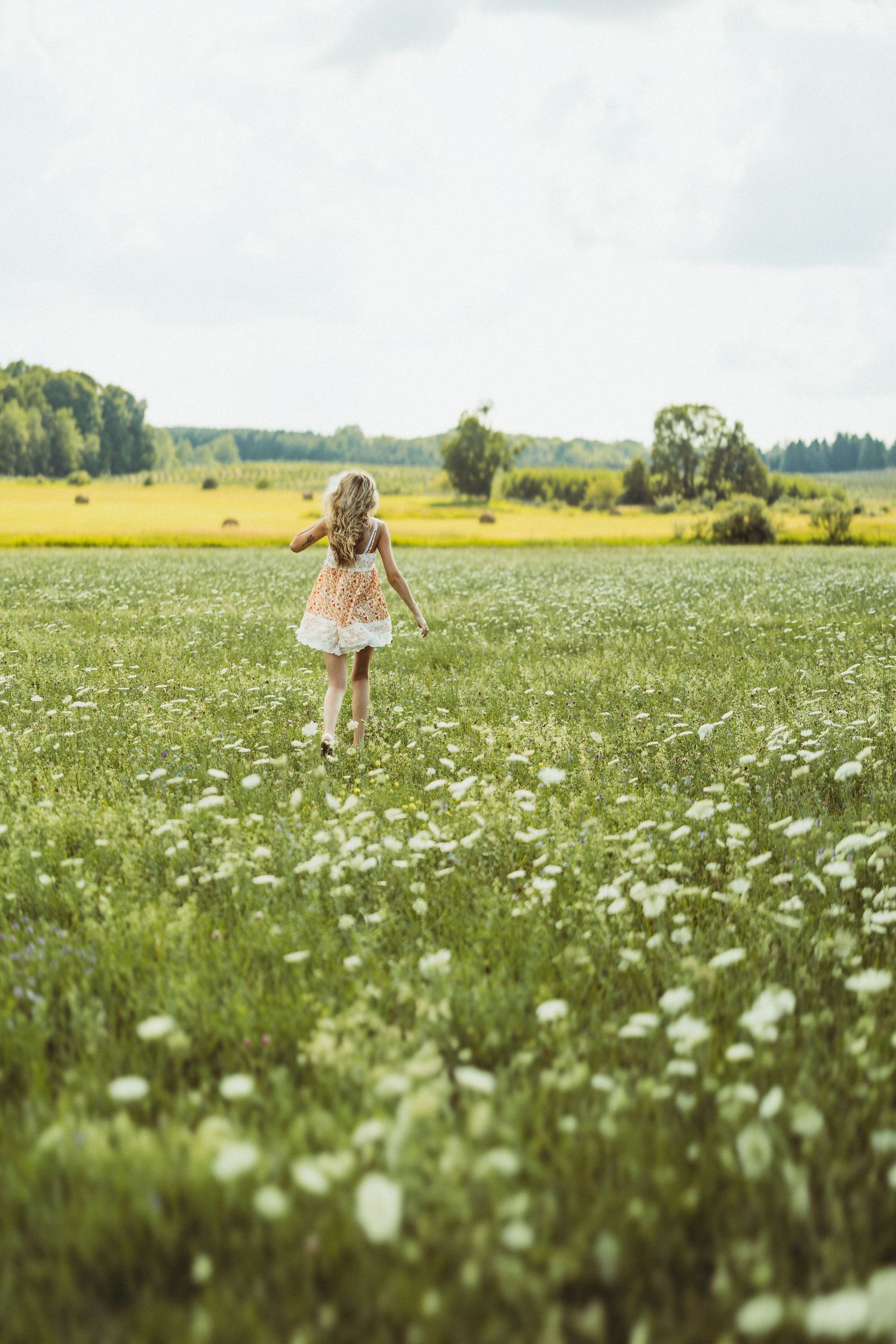 A figure in a flowy dress walking through a meadow filled with white wildflowers.