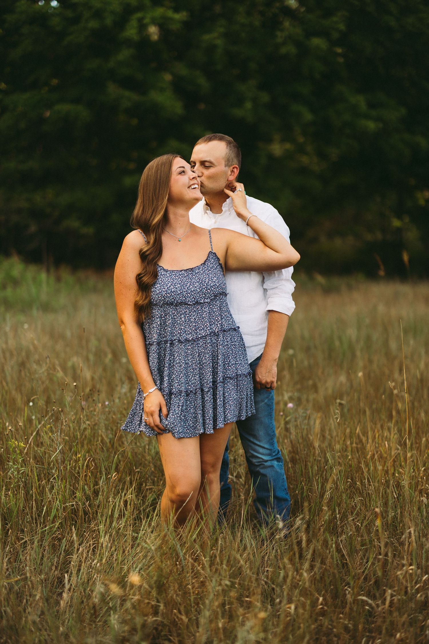 Couple in summer outfits sharing playful moments in tall grass field.