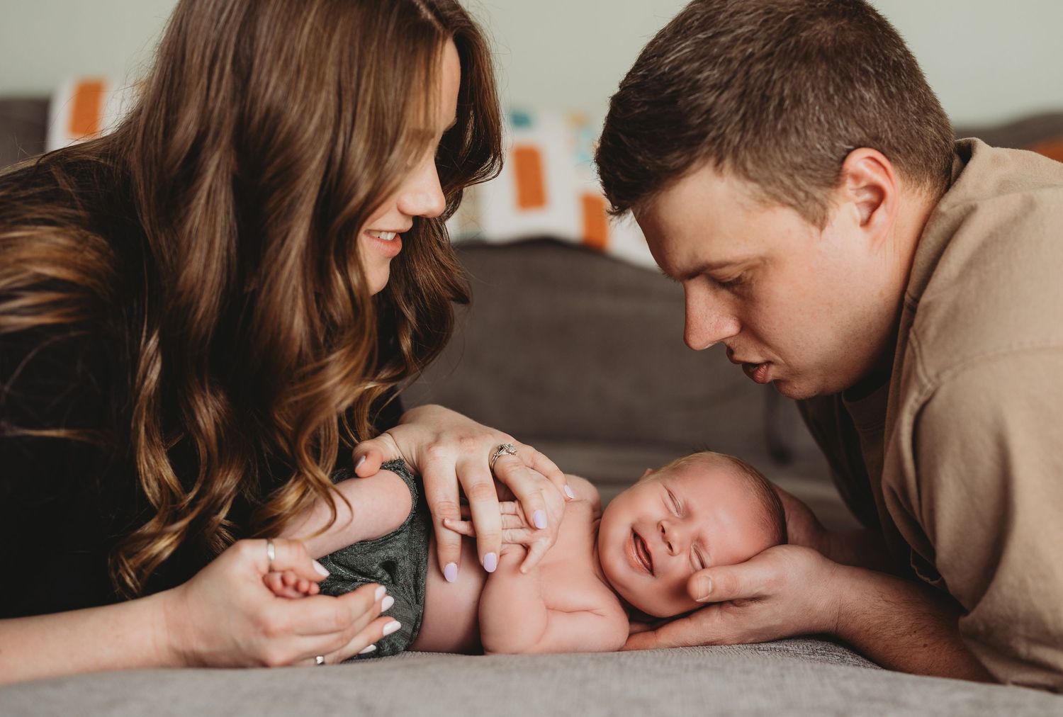 Intimate lifestyle newborn photography session with parents on grey bedding.