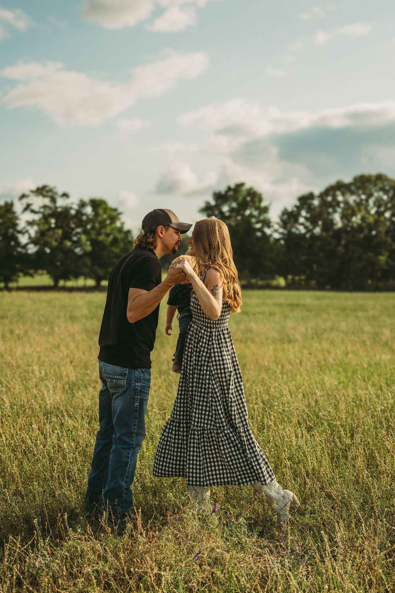 A couple dancing together in a sunlit meadow with the woman wearing a checkered dress.
