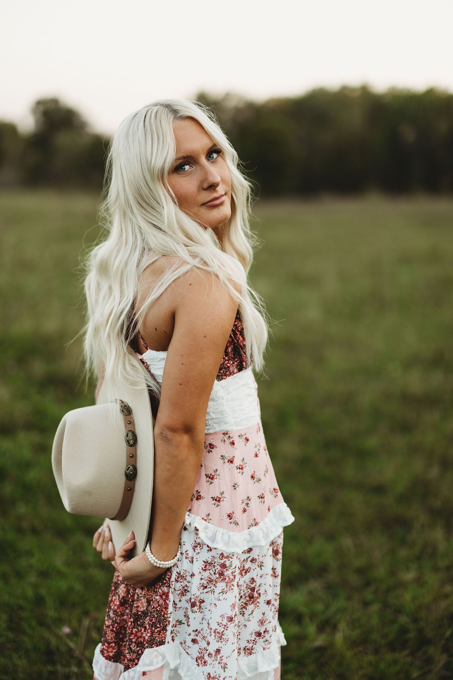 Summer fashion portrait in a floral dress with white backpack in a grassy field.