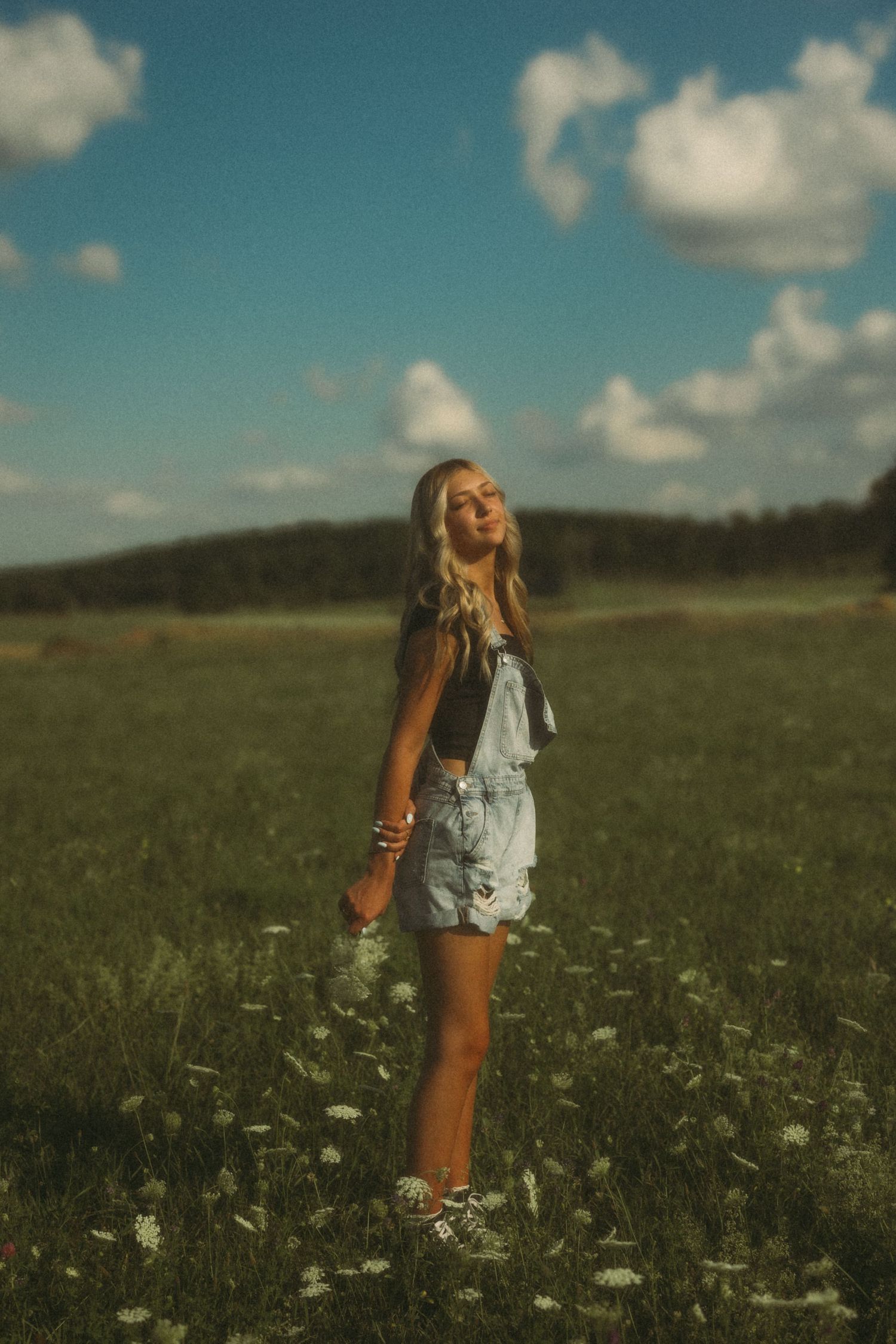 A dreamy summer portrait of someone in overalls standing in a wildflower meadow at sunset.