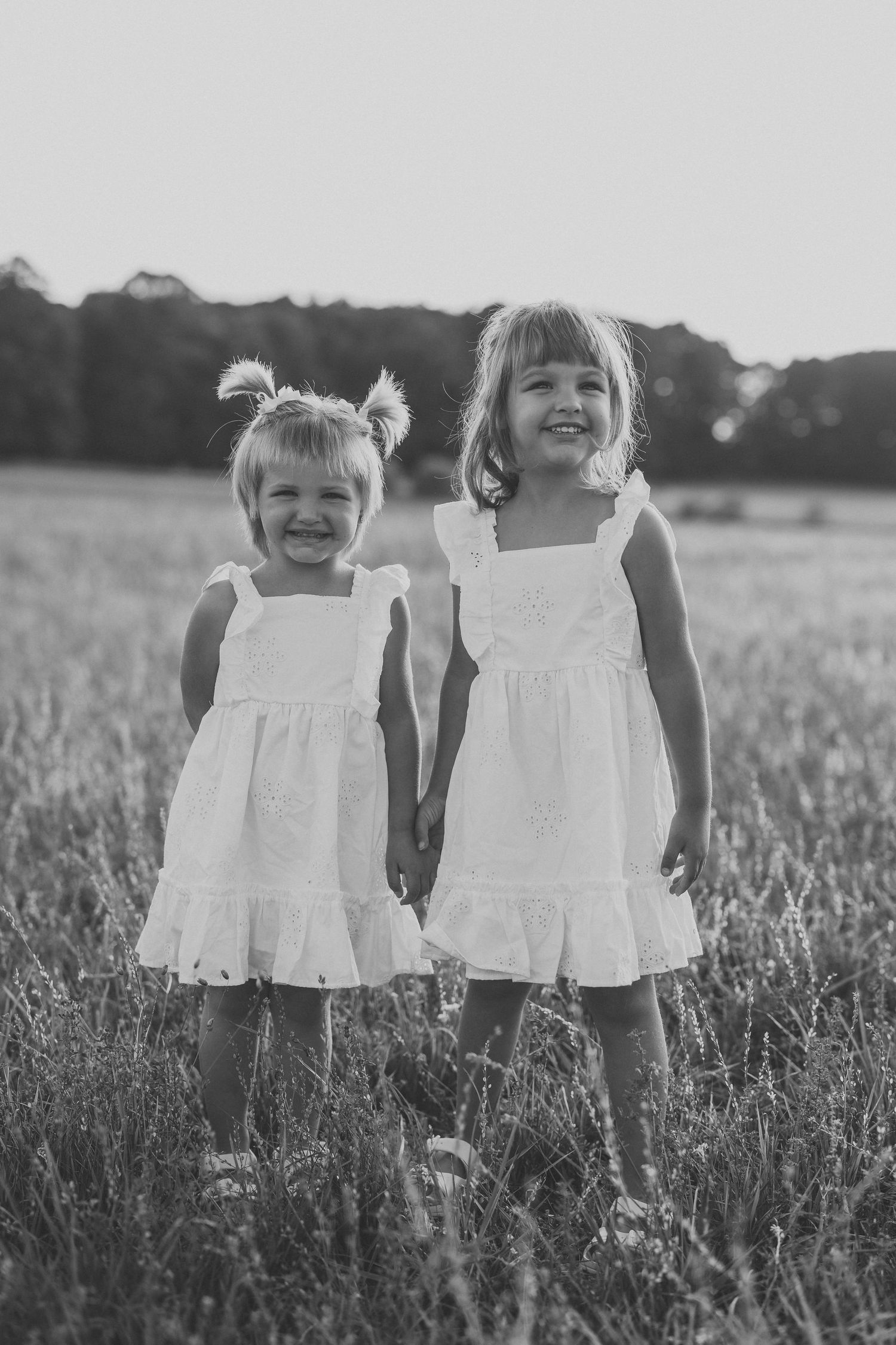 Black and white image of two children in white dresses standing in a meadow.