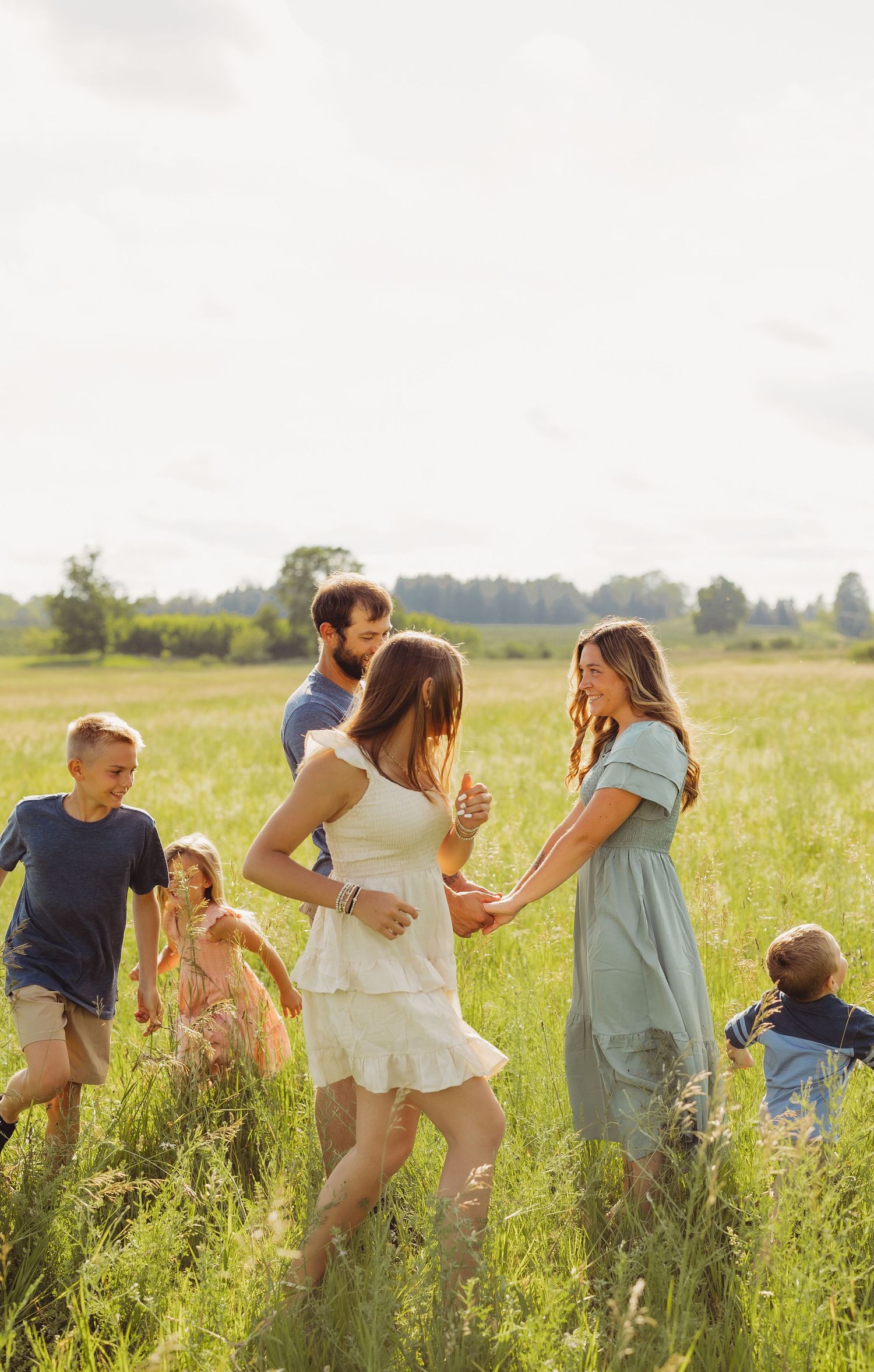 Family dancing together in a sunny green field, with children and adults holding hands in a joyful outdoor setting.