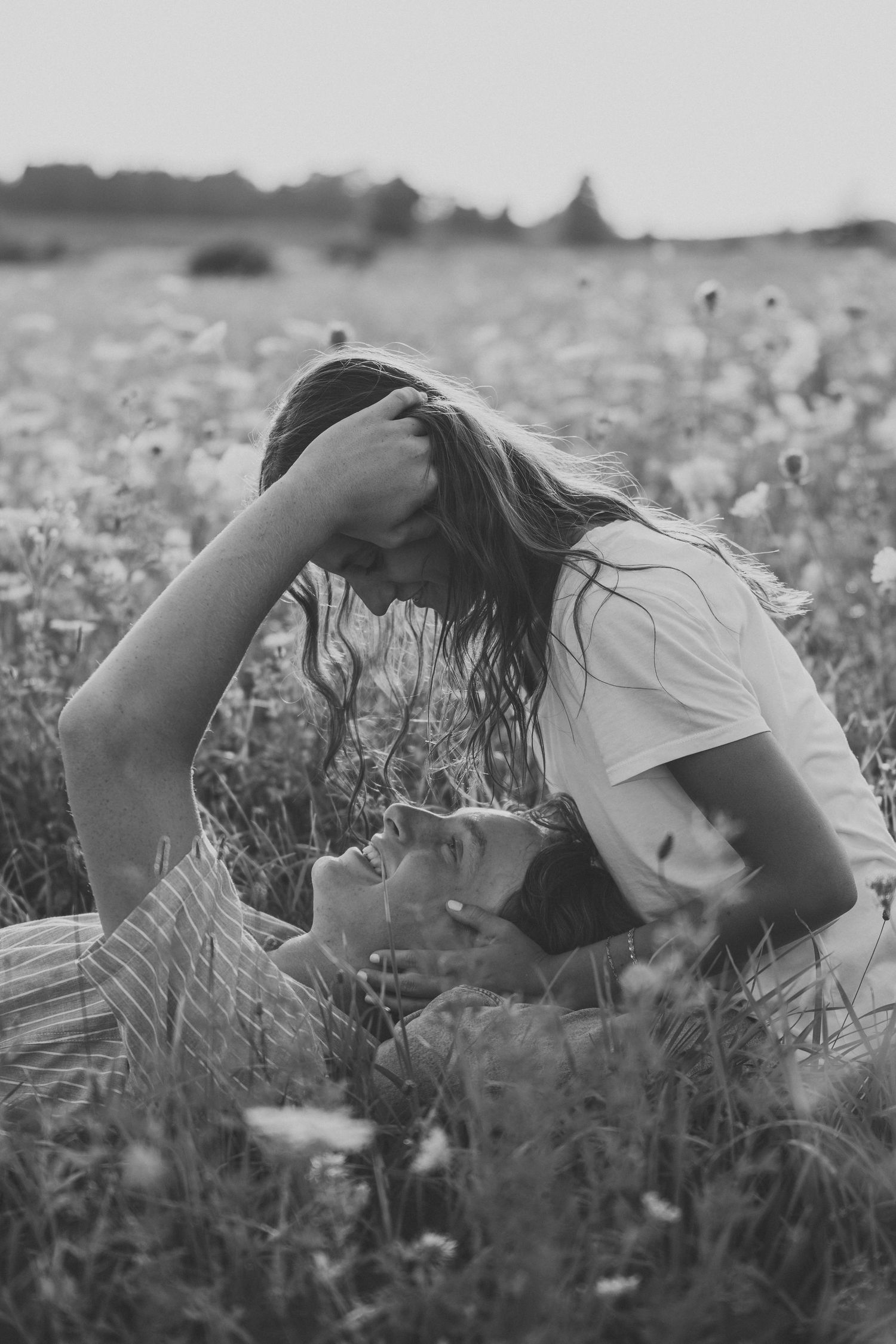 Black and white photo of romantic couple lying in wildflower field, tender intimate moment outdoors.