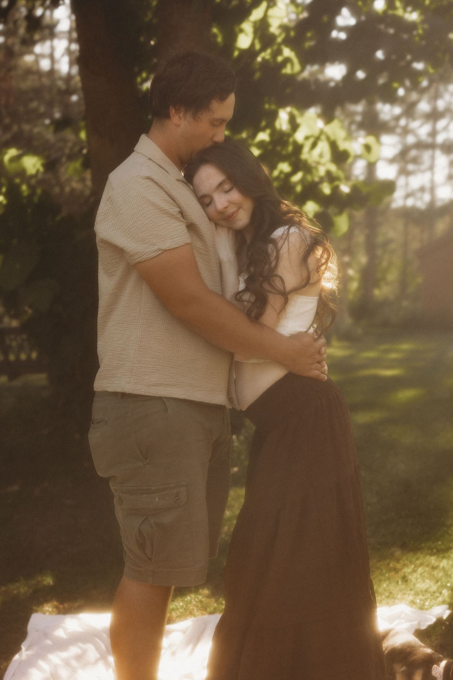 Couple embracing tenderly under a tree in warm golden hour sunlight in a lush garden.